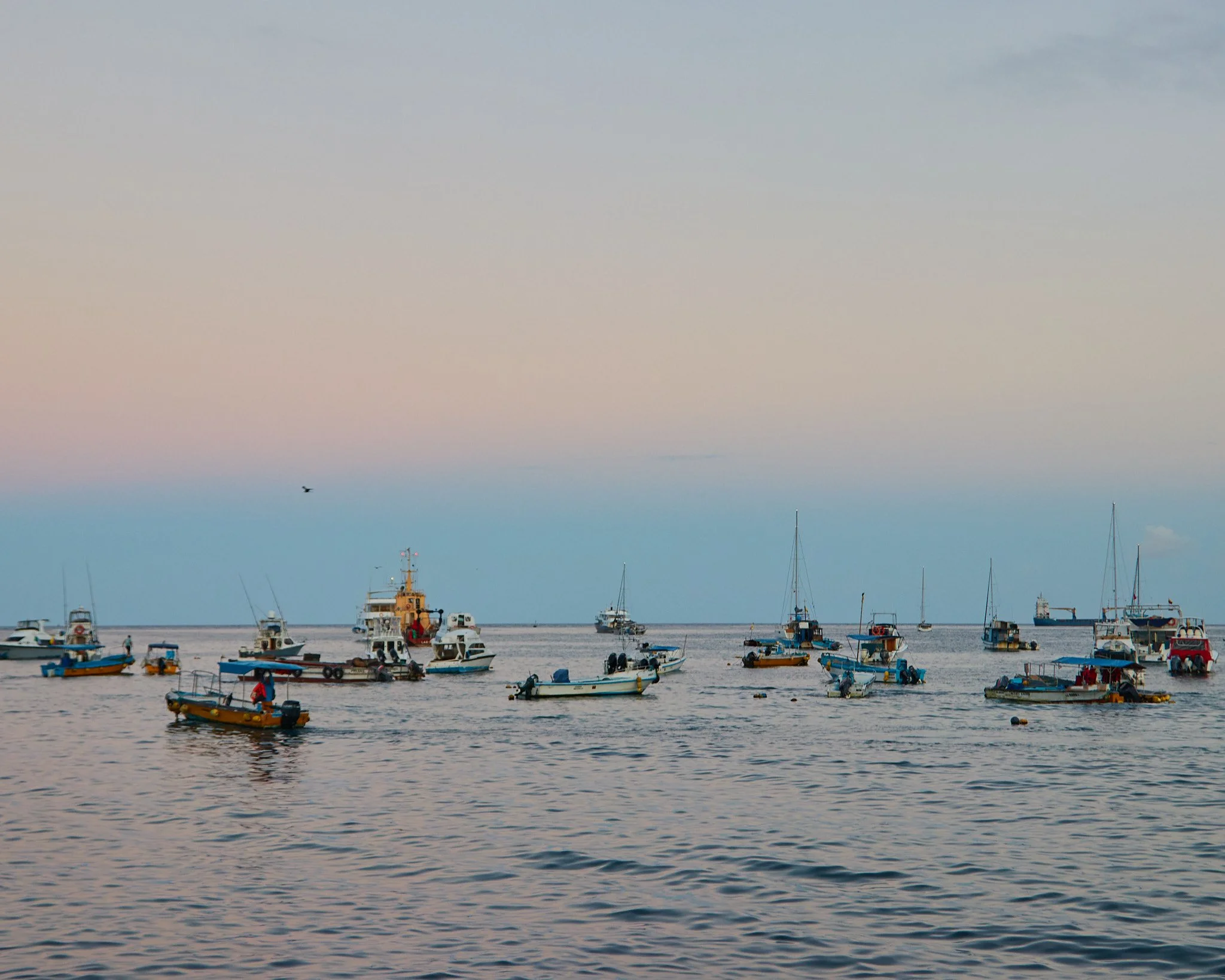Fishing boats and sailboats anchored in the harbor of Puerto Baquerizo Moreno at dusk