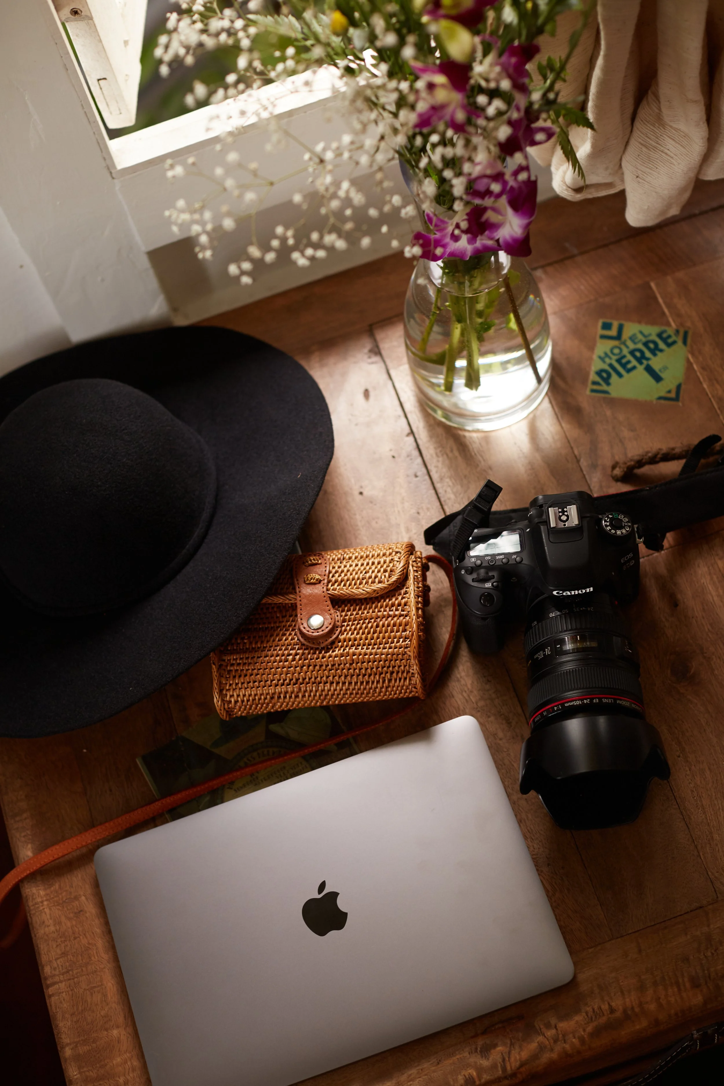Wooden desk with laptop, camera, purse, hat, and flowers