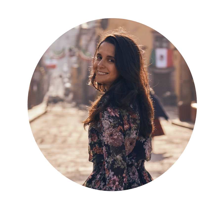 Karen Gomez, founder of Passport in Photos, smiling over her shoulder in a floral dress on a cobblestone street lined with Mexican flags