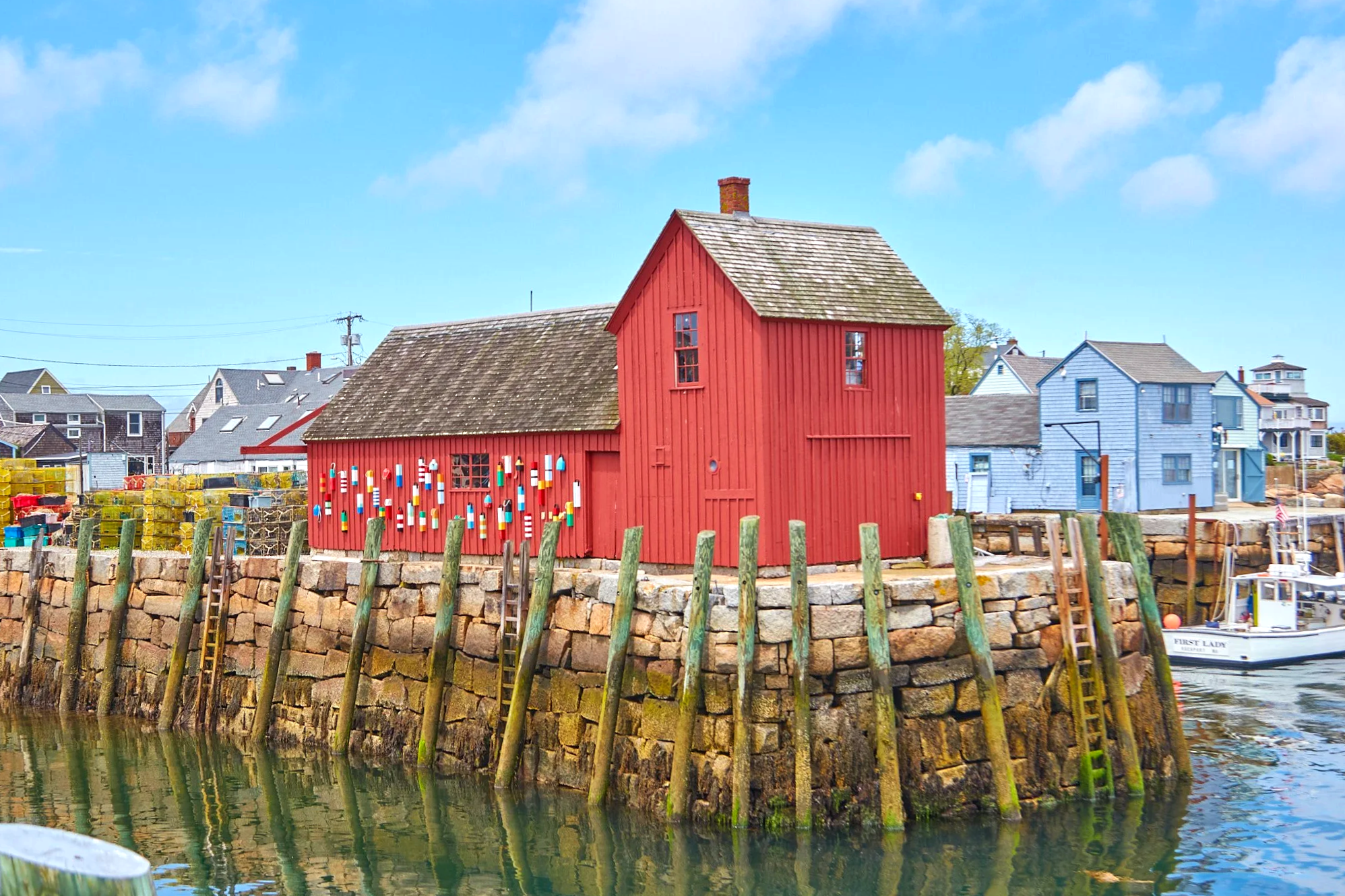 Motif No. 1 red fishing shack at Bradley Wharf in Rockport, MA with lobster traps, wooden pilings, and harbor water on a clear day