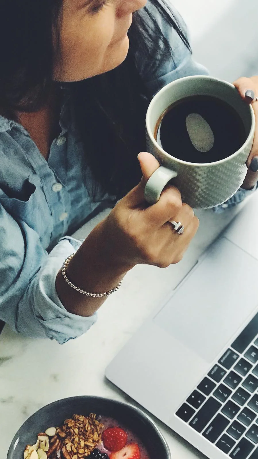 Overhead view of a travel advisor planning a trip on a laptop with coffee and a breakfast bowl