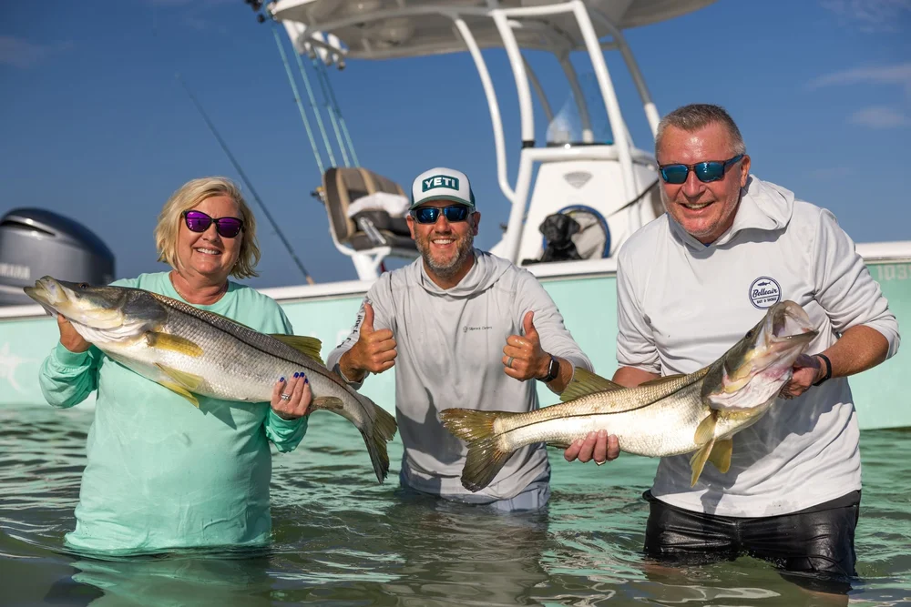 Two happy anglers holding snook in shallow water with Capt. Phil