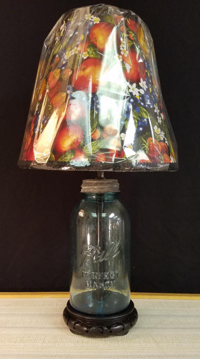 Antique Ball Jar Lamp "PERFECT MASON" Caning Jars are very collectible at this time, and finding creative ways to display them is part of the challenge. We do not use a craft kit to make this lamp, it is drilled and mounted to a wood base with the electric wire coming out the bottom. Complete with a Vintage Zinc lid. With a little bit of disassembling, it could be opened up and filled with items. Since we manufacture every lampshade we sell, we purchased some fruit print fabric to make the lampshade. Buyer may select a traditional fabric lampshade, if desired. It stands 21" tall, including the lampshade. $160.00, plus shipping