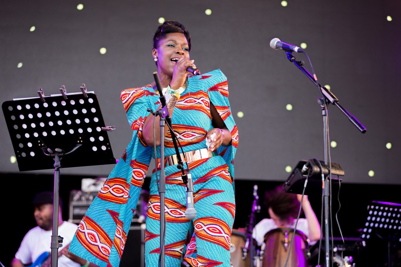  A lady in bright african print sings into a microphone on stage 