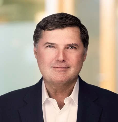 Professional headshot of a man in a dark suit and white shirt, with a blurred background.
