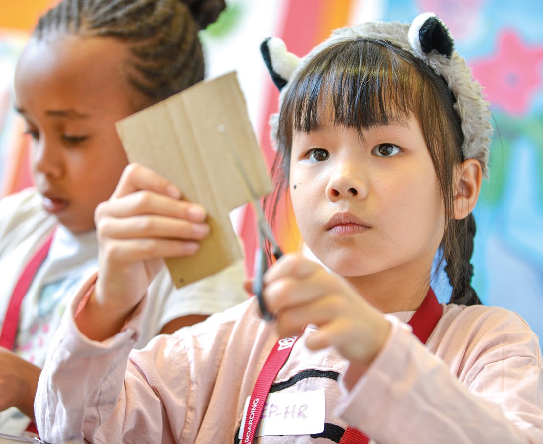 Female student cutting carboard for a craft activity at camp dragon.jpg