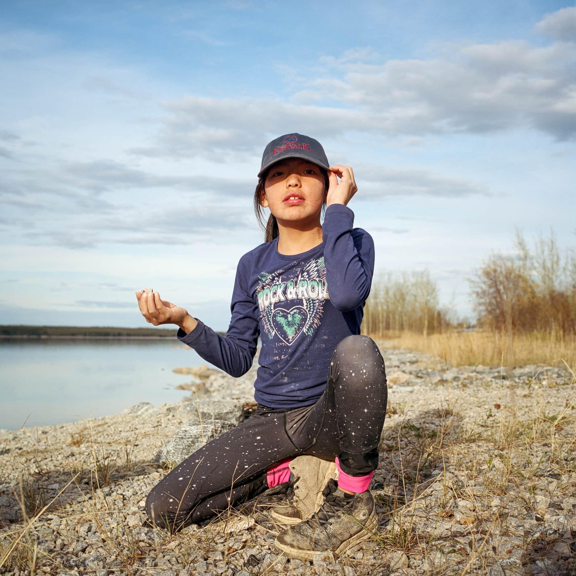 Aalaiyah wears a Keeyask hat while she plays on riprap-enforced river banks that surround the community of Split Lake, 60 kilometres upstream of the dam. Elders often speak about how they used to swim and play in the shallow waters, catching crayfis…