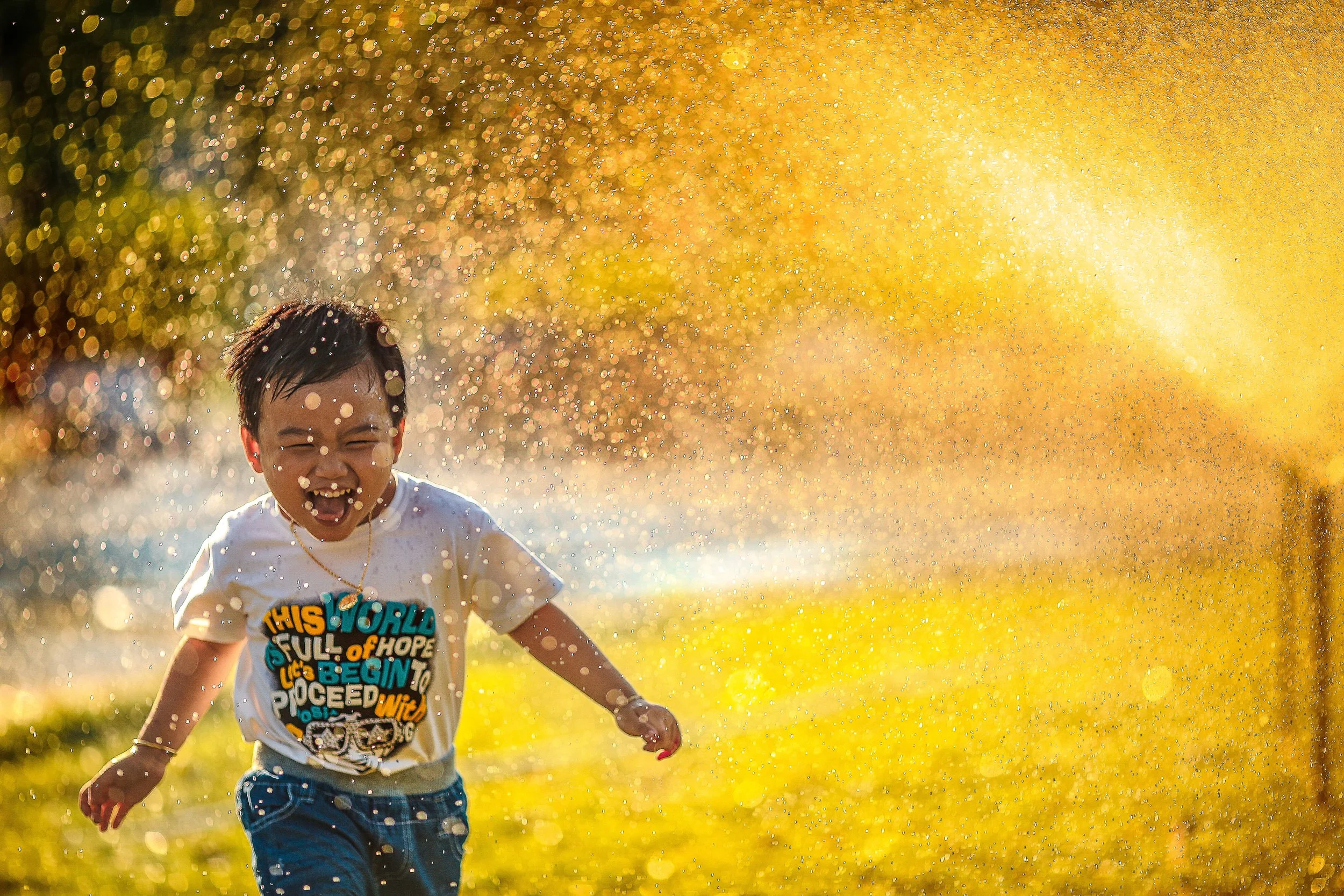 Child running and laughing through a sprinkler.
