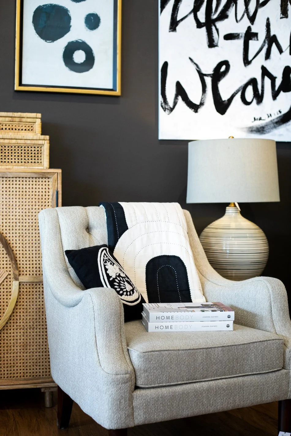 Living room with beige armchair, black and white decorative pillows, wooden furniture, abstract wall art, and a large striped table lamp.