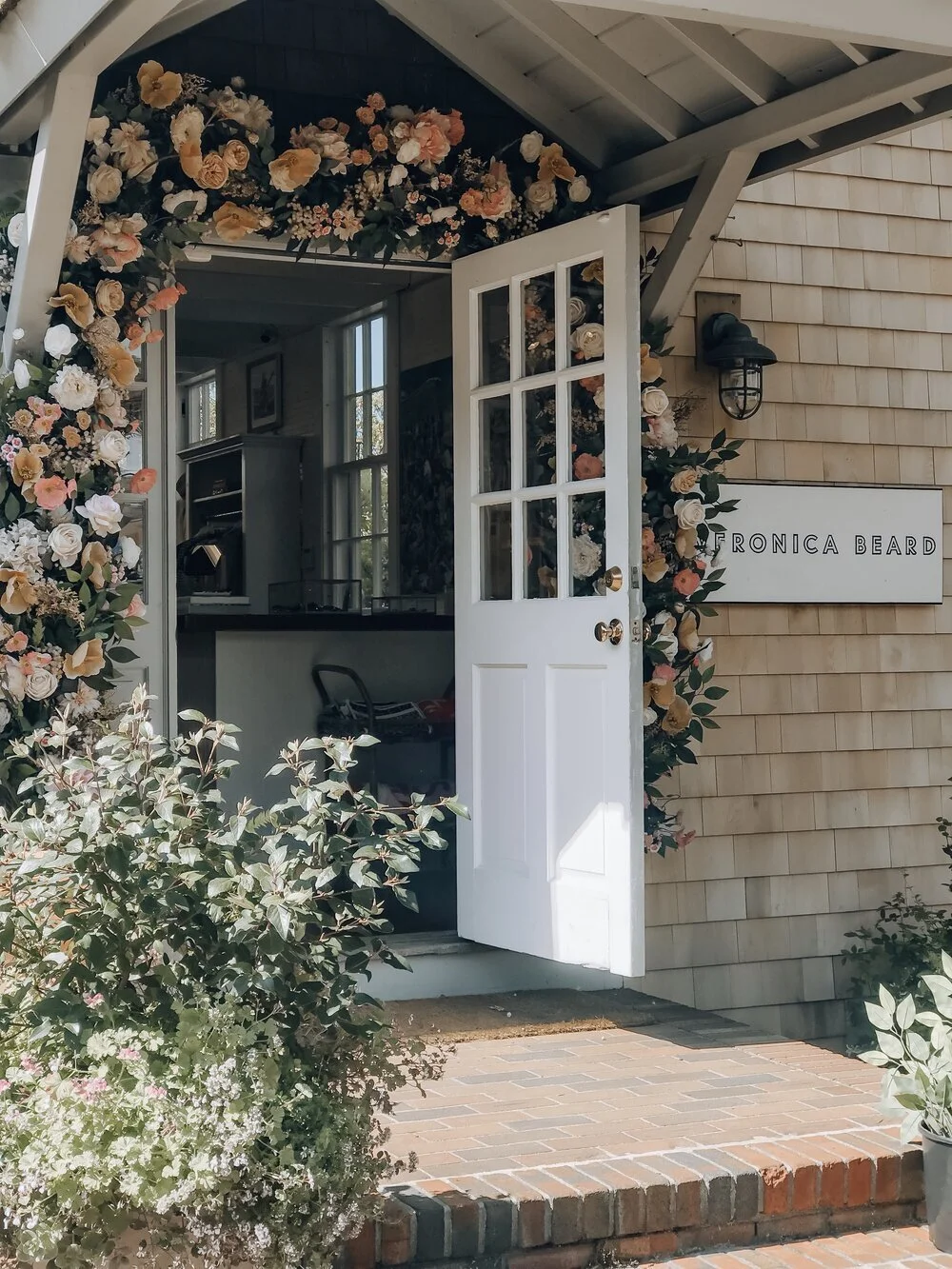 Open door of a shop with a floral wreath, sign reading 'Veronica Beard', and interior visible through the door.