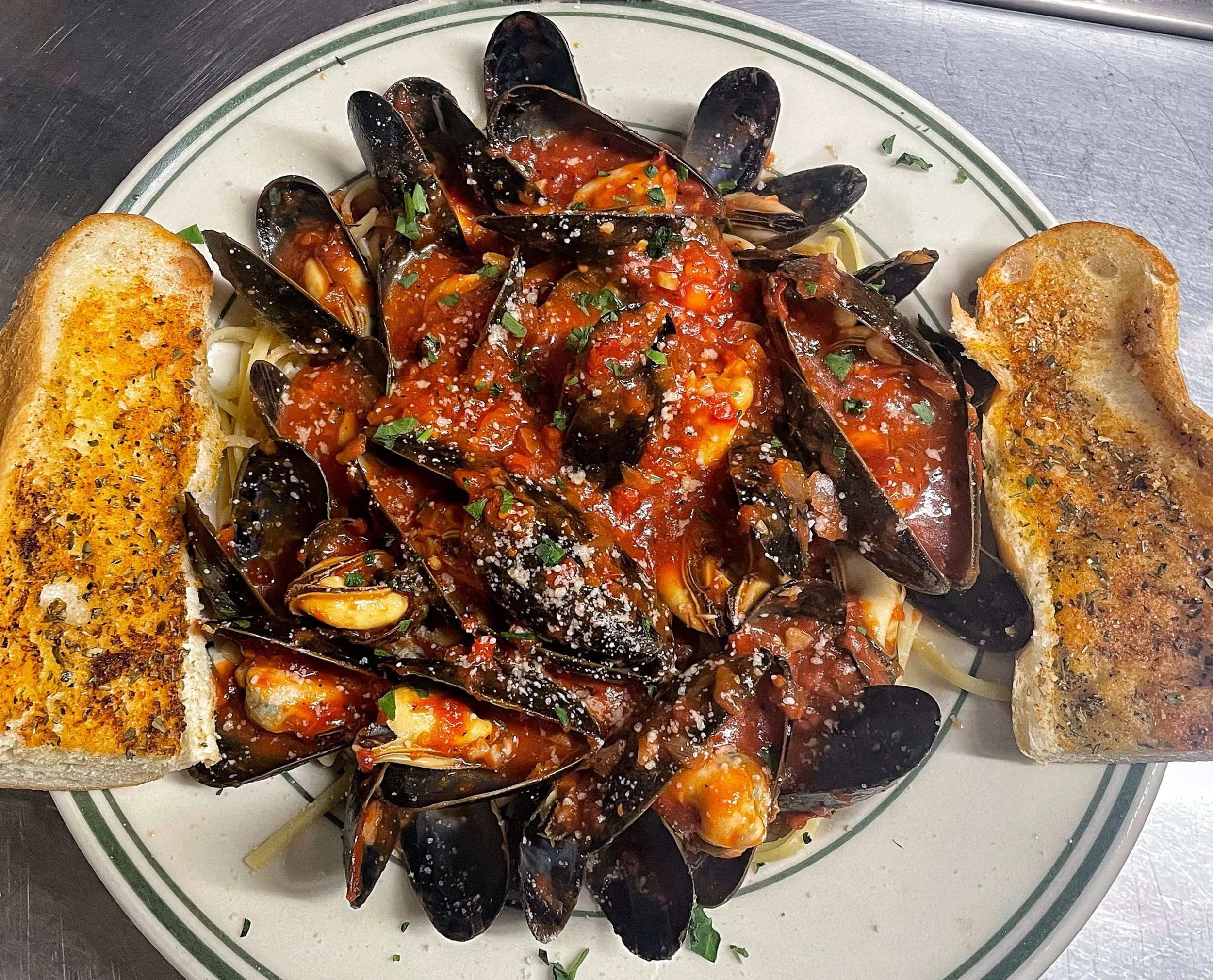 Fresh Maine mussels sautéed in marinara sauce over linguine at John & Molly's Tavern in Eastampton, NJ – piled high with plump mussels, rich tomato sauce, chopped parsley, grated Parmesan, and served with toasted garlic bread on the side.