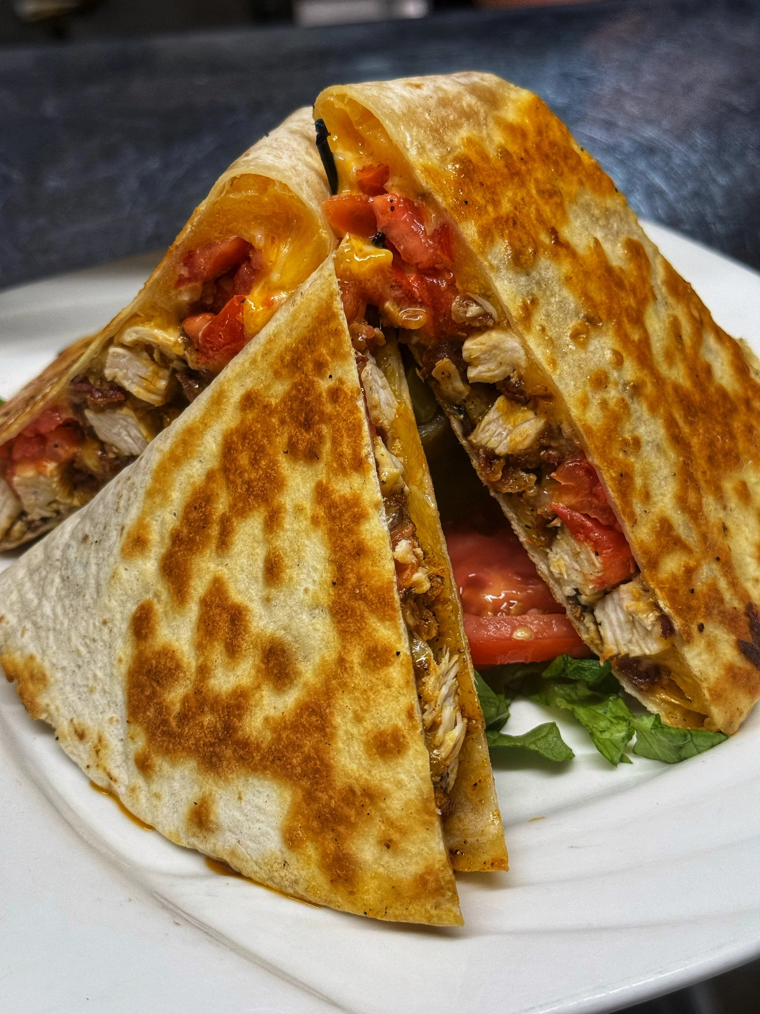 Golden, grilled Cajun Chicken Quesadilla at John & Molly's Tavern in Eastampton, NJ – stuffed with seasoned grilled chicken, melted cheddar cheese, sautéed peppers, onions, tomatoes, and served in crispy tortilla triangles with fresh side greens.