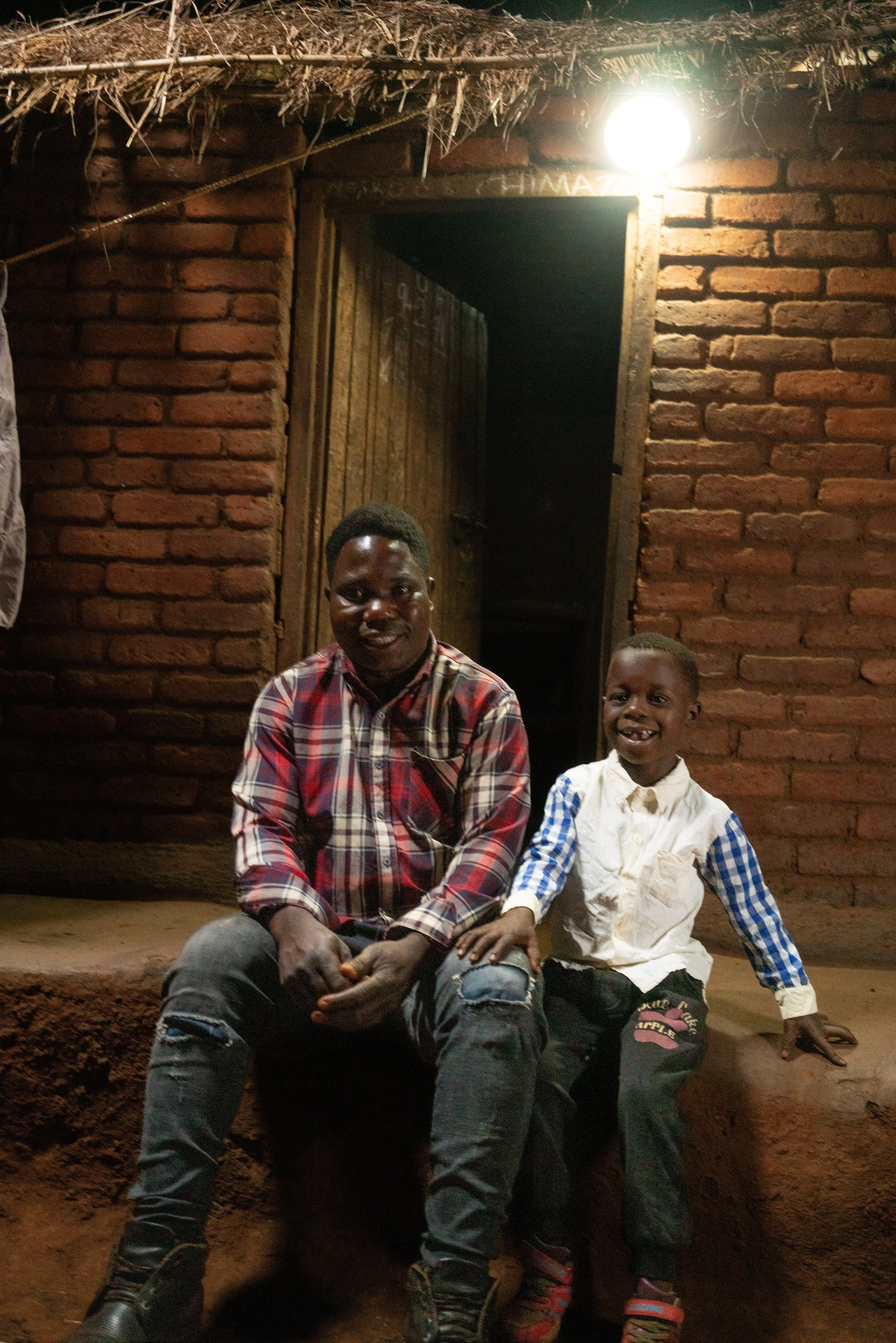 Benedicto and his son sit outside of their home under their solar light. Photo Credit_ SolarAid_Chris Gagnon.jpg