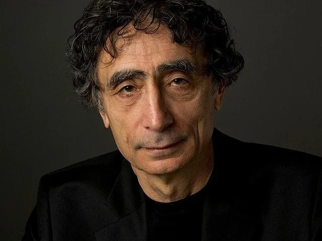 Middle-aged man with curly hair in a black jacket against a dark background.