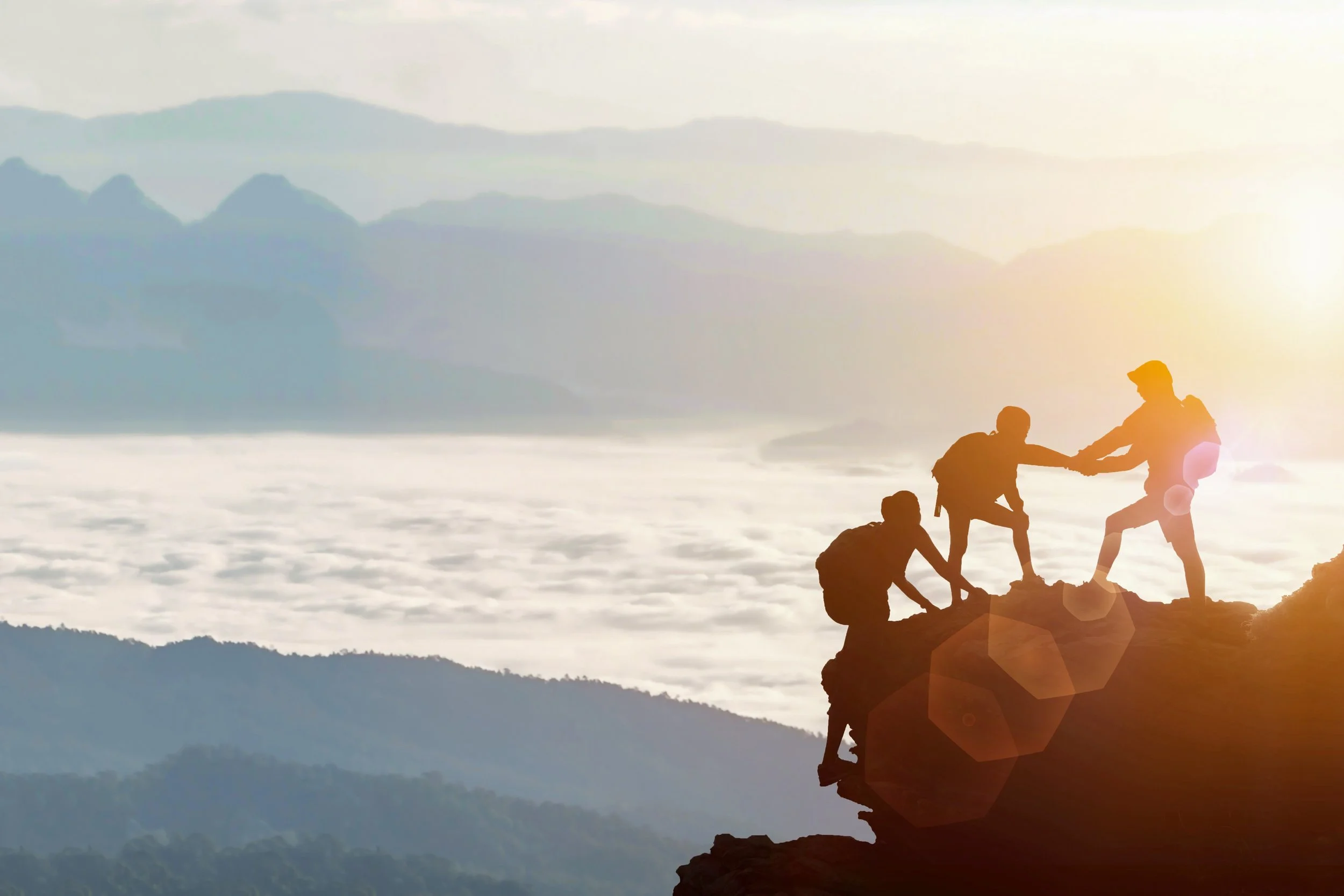 Person supporting others up a mountain path at sunset, symbolising guided support and resilience in therapeutic work