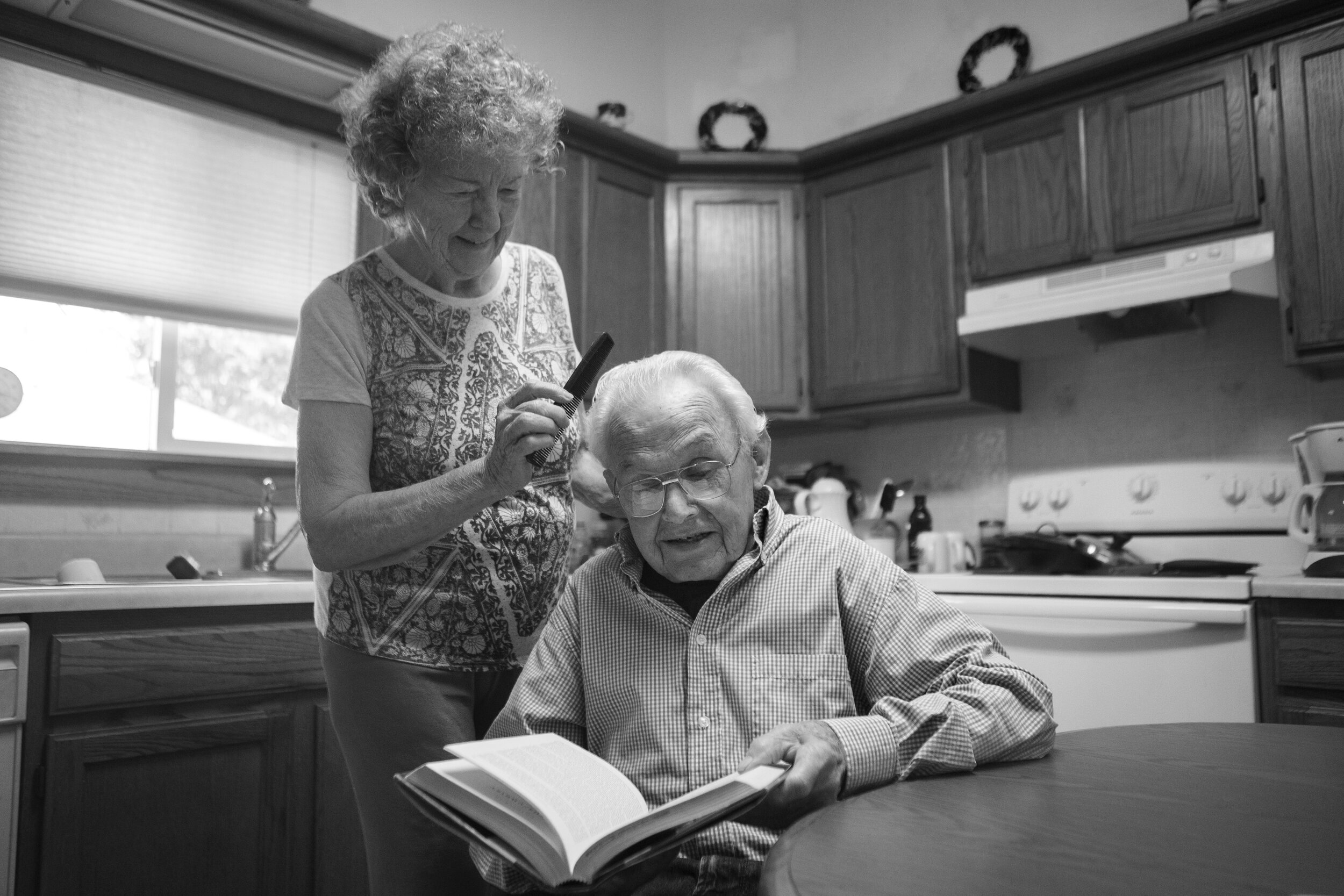  Jean Krejci (left) combs the hair of her husband John Krejci, in their kitchen while he reads a book at their Lincoln home on Monday, August 24, 2020.  Krejci previously served as a priest and later married a Jean who was a nun. Both have spent thei