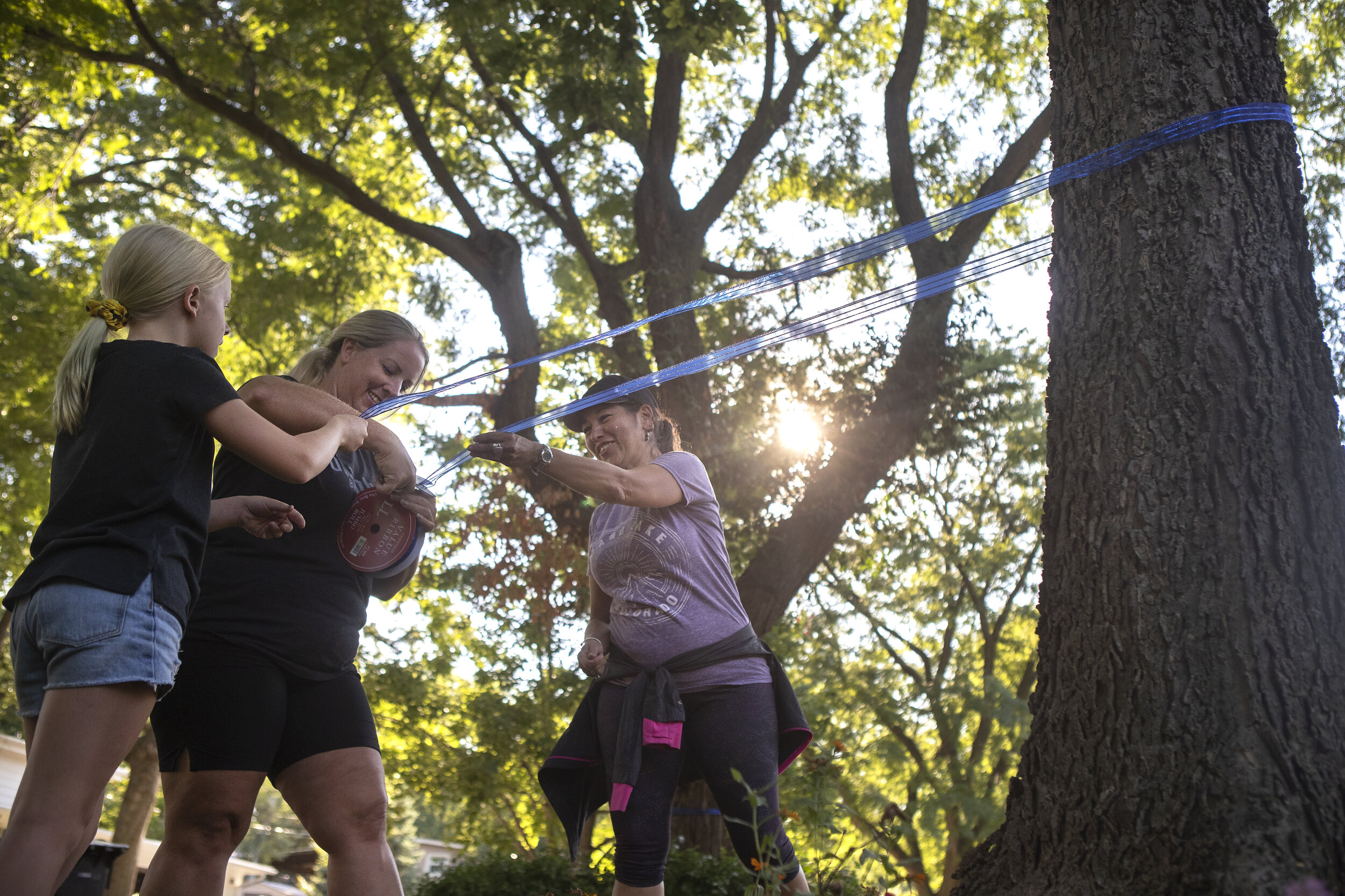  Elsa Gauksson,  Kendra Gauksson, and Kathy Ponte (from left) tie blue ribbons around trees in the Eastridge neighborhood where Mario Herrera lives to show their support for the LPD officer and his family on Monday, August 31, 2020, in Lincoln, Nebra