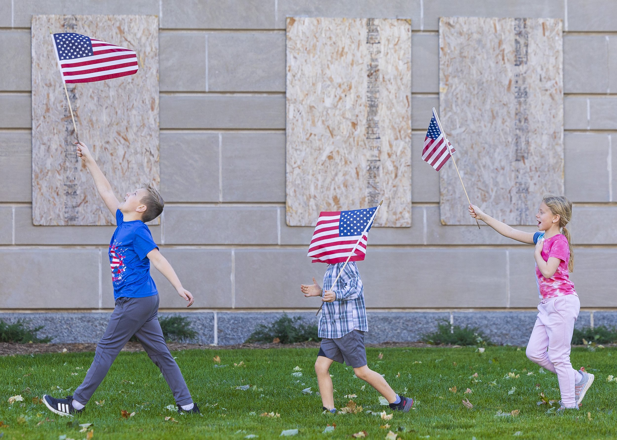  Henry Gonnerman, 10, Augustine Milana, 7, and Iris Gonnerman, 7, (from left) parade their flags outside the Capitol while belting out the chorus of America the Beautiful before the start of the Lincoln Veterans Parade, on Sunday, Nov. 12, 2023.  