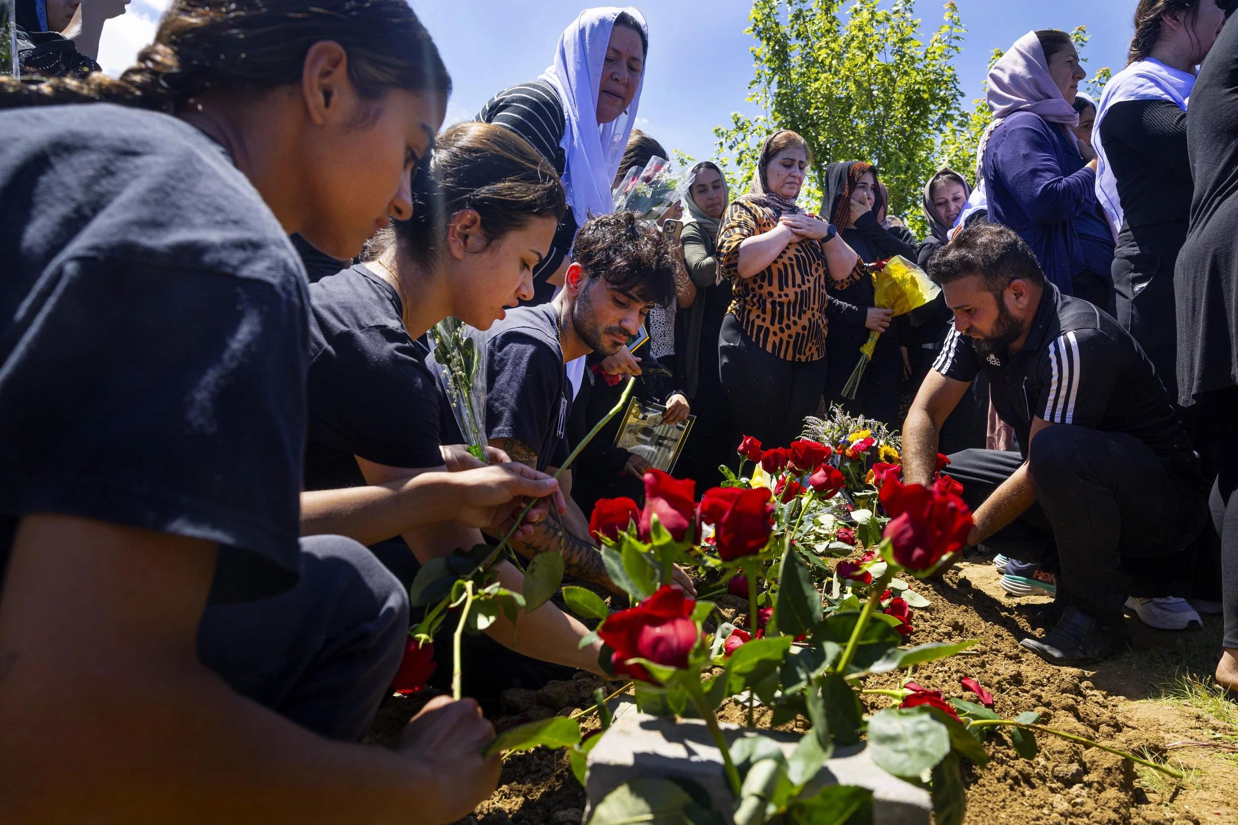  Members of the Yazidi community place roses on the grave of Karwan Breem during a funeral held for Karwan and his sister Carolin at the Yazidi National Cemetery on Tuesday, July 1, 2025, in Malcolm.  On Monday, Karwan Breem, 18, was driving a Cadill