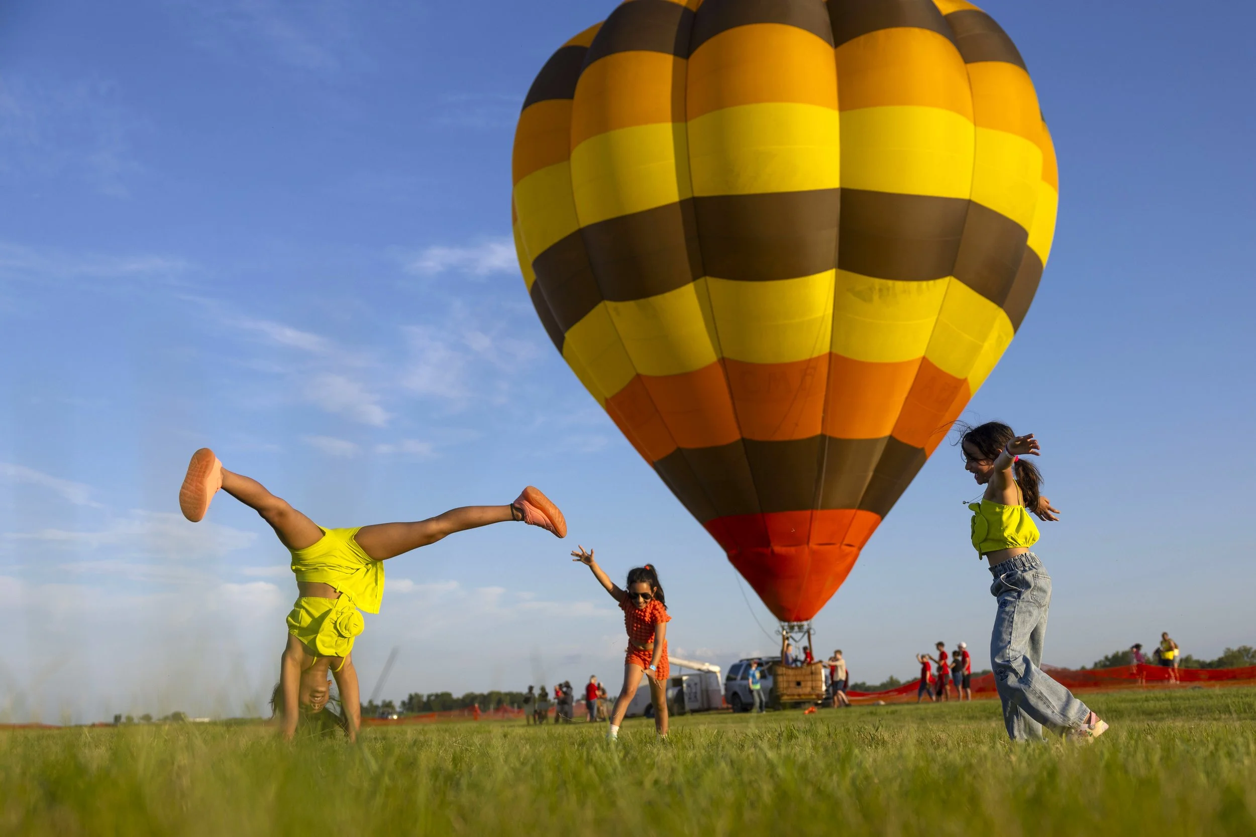  Anaya Agarwal, Avya Agarwal and Sanvi Manchikalapati (from left) perform cartwheels in front of the Balloon "Retro" flown by Darrin Harrison (not pictured) during the Hot Air Balloon Festival held at Brenner Field on Friday, June 13, 2025, in Falls 