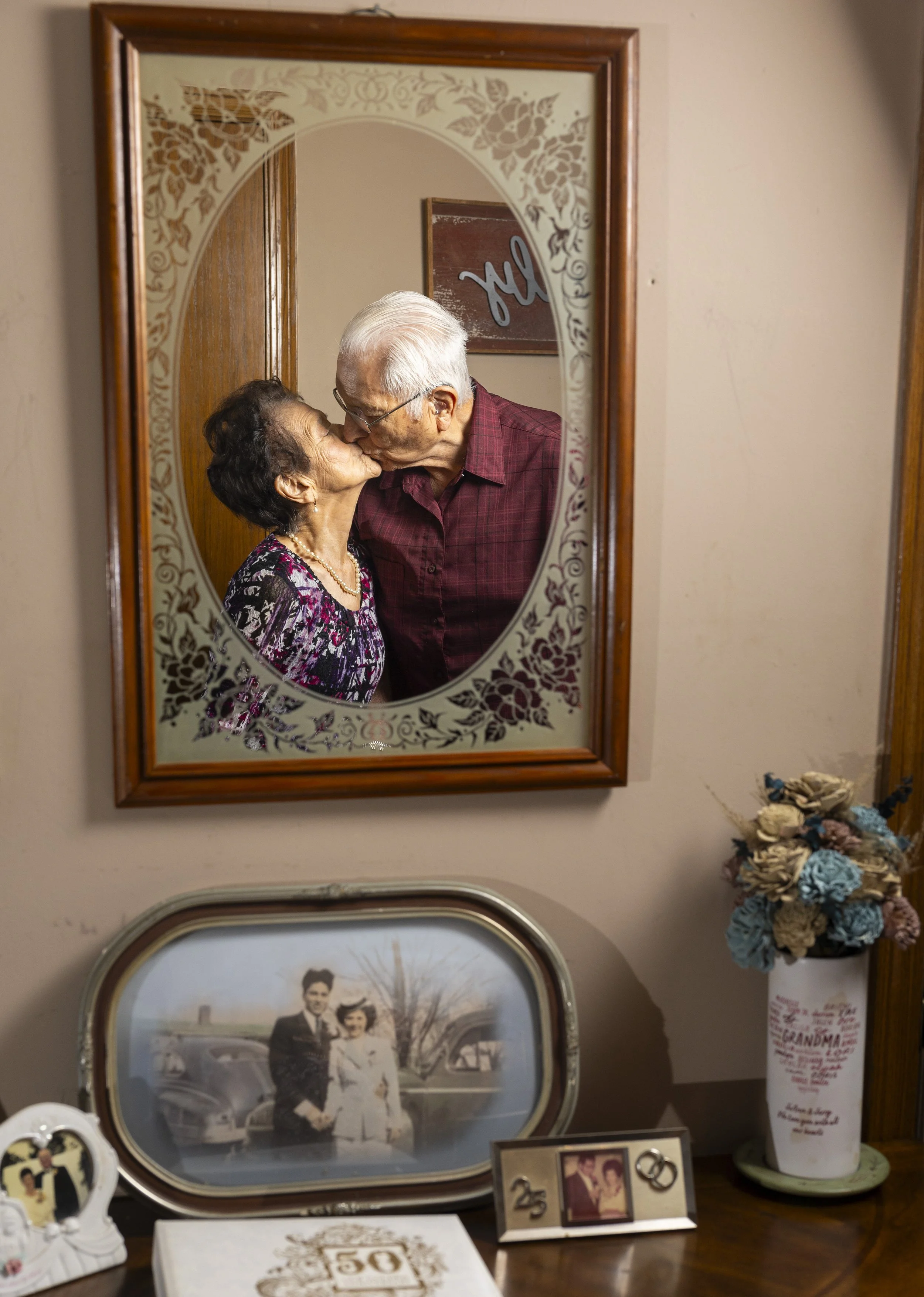  Ignacia Hernandez, 90 (left), kisses her husband Chris, 95,while they are reflected in a mirror that hangs over photos from their time together at their home in south Lincoln, on Tuesday, Feb. 6, 2024. The couple is celebrating their celebrating the