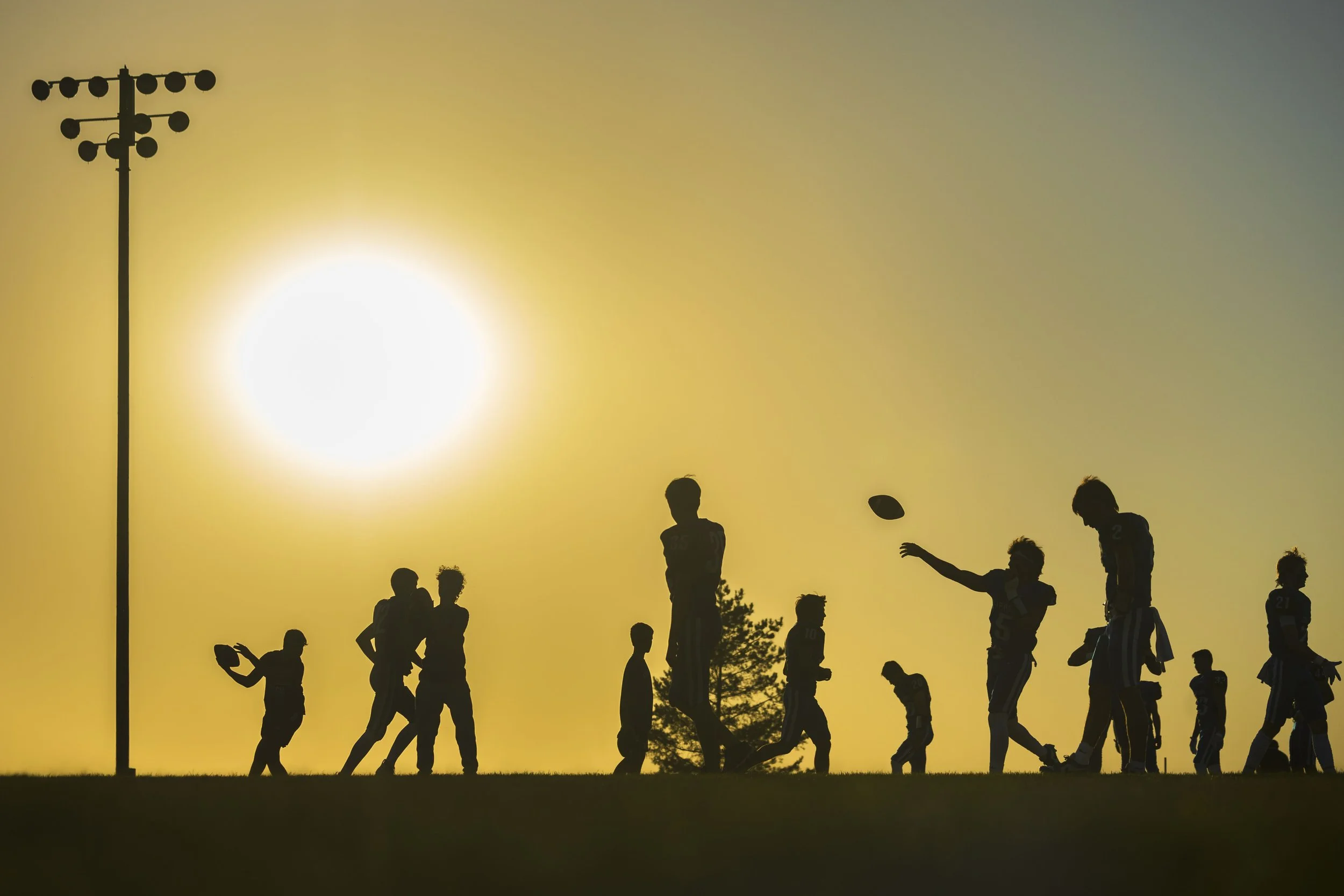  Malcolm players are silhouetted by the sun as they warm up before their game against Bishop Neumann on Friday, Oct. 4, 2024, at Malcolm High School.  