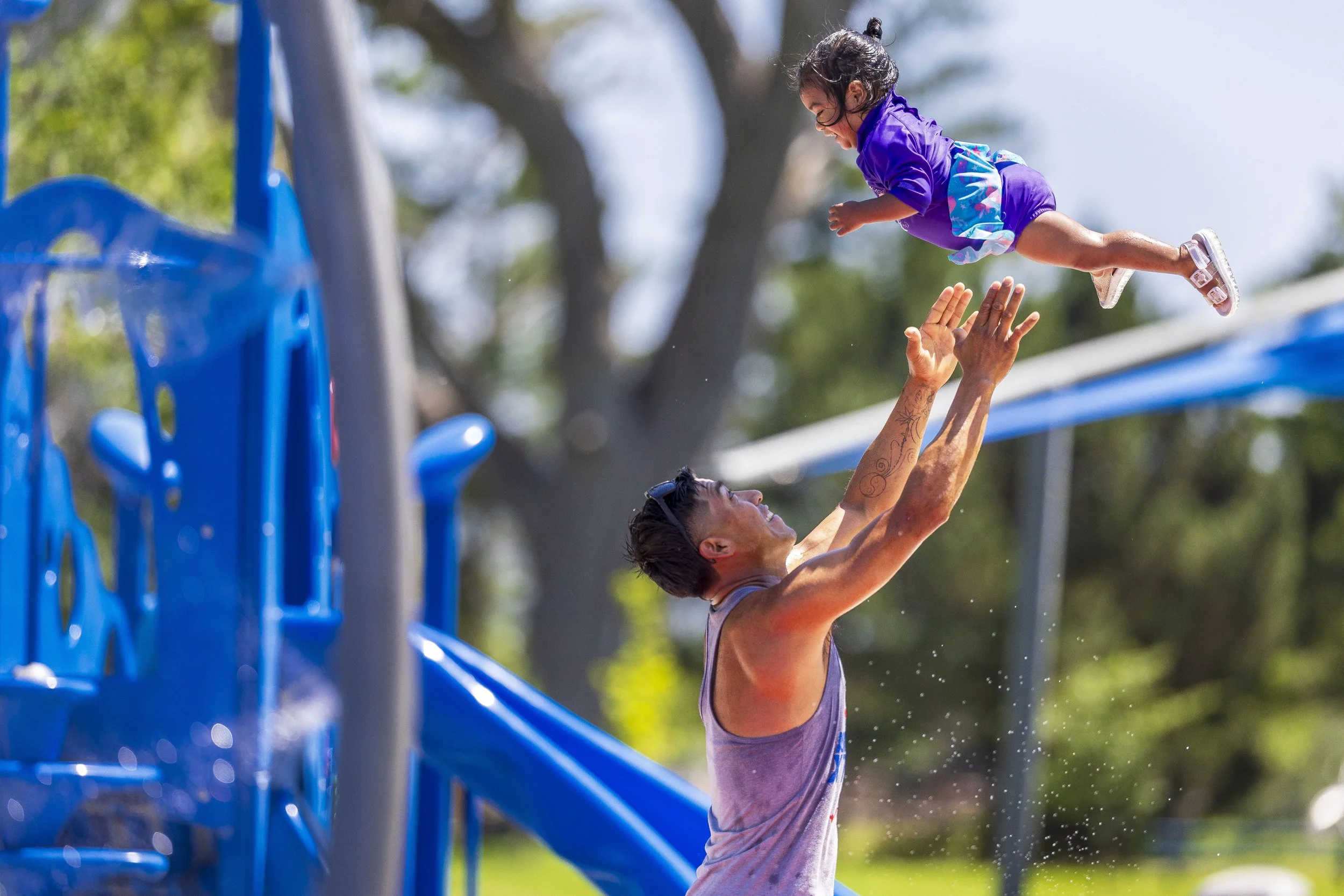  Luis Hernandez tosses his daughter Amor into the air as they play together at the Trago Park Sprayground on Friday, June 20, 2025, in Lincoln. Lincoln is under an extreme heat warning through Sunday night. 