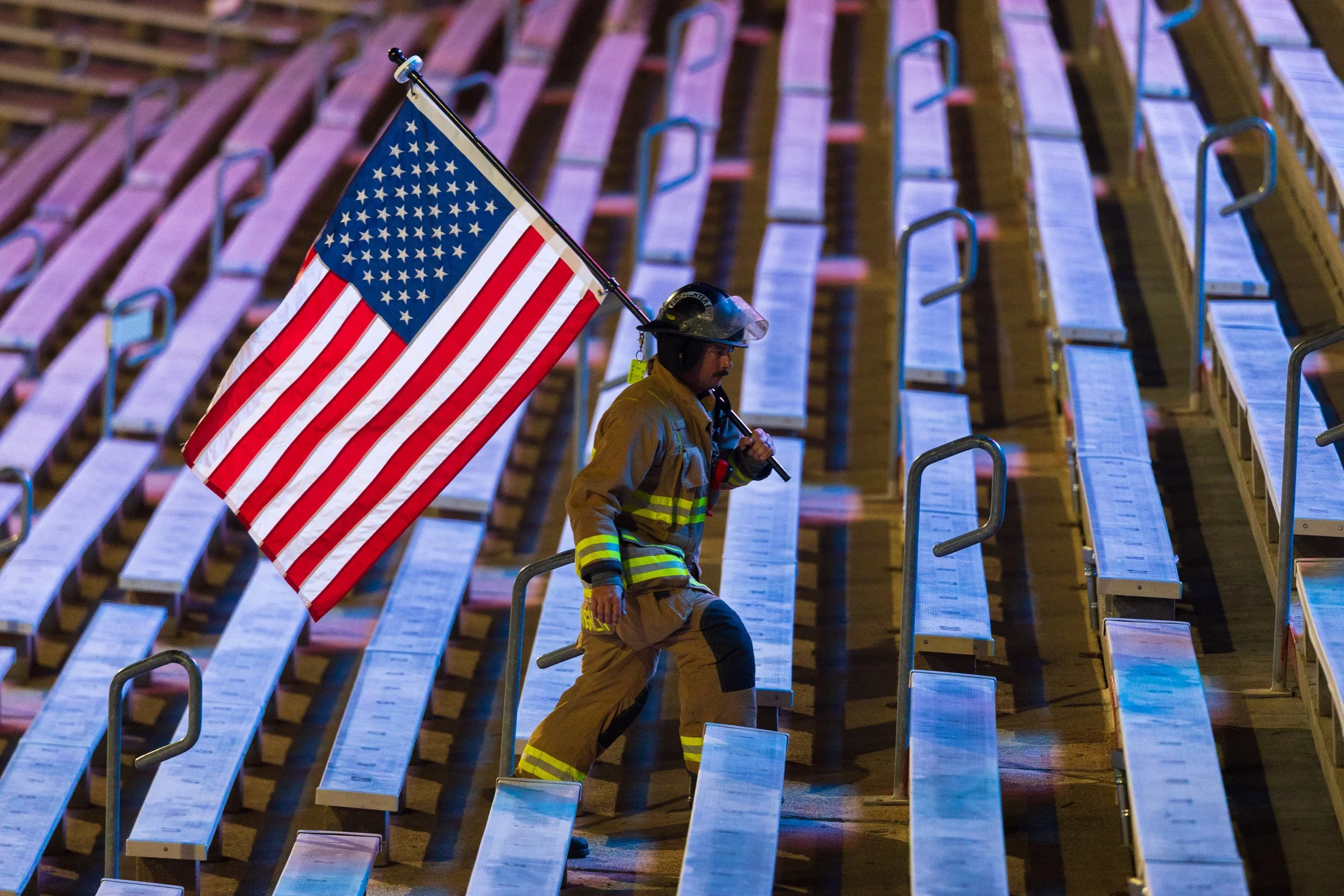 Crete firefighter Tim McLaughlin carries an American flag up the north stadium steps during the 9/11 memorial stair climb on Friday, Sept. 11, 2026, at Memorial Stadium.