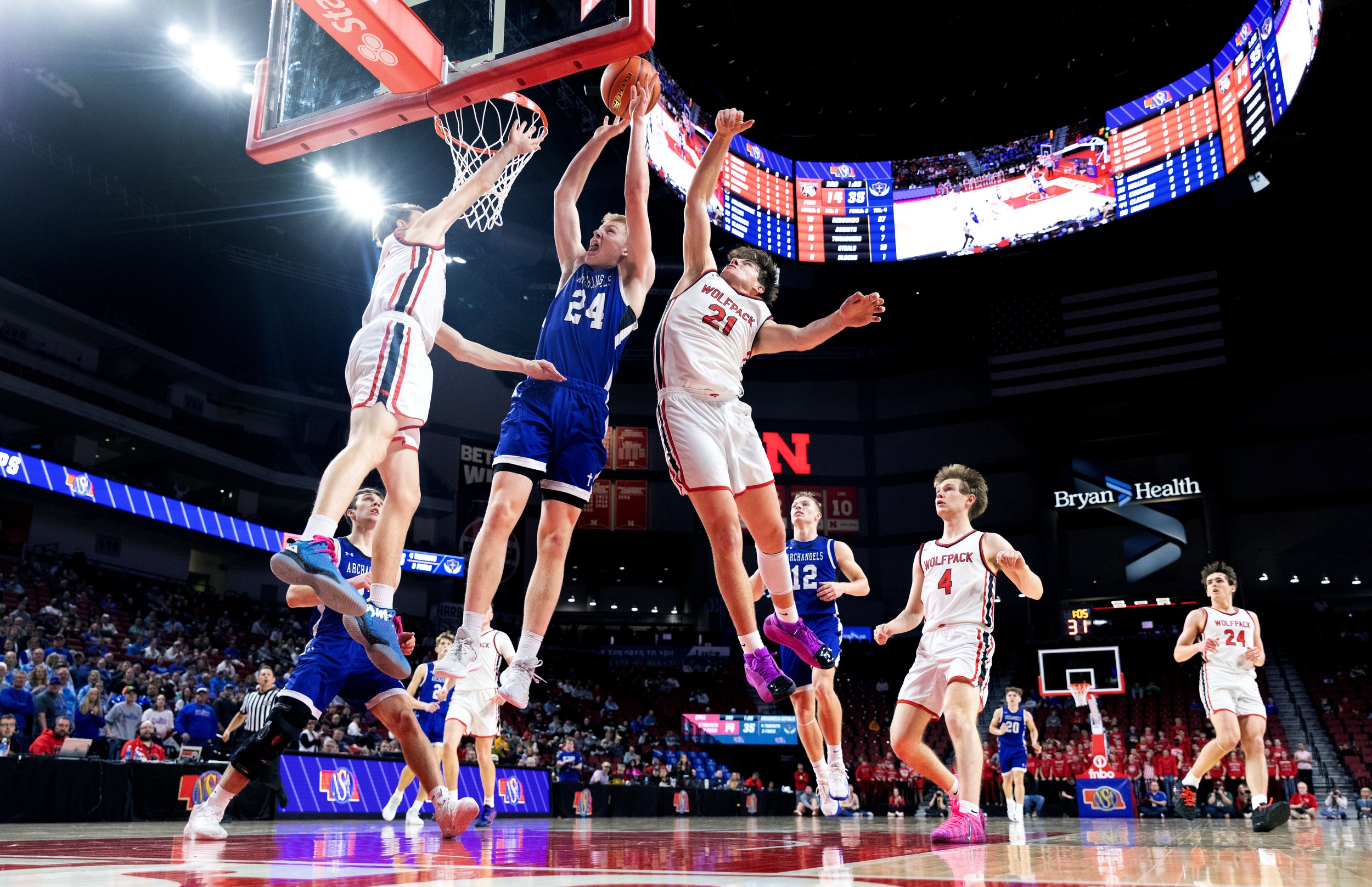 Elgin Public/Pope John’s Evin Pelster (12) and Jarek Erickson (21) defend Archangels Catholic’s Kellan Mundil (24) as he goes up to score two during the Class D-2 championship state basketball game on Saturday, March 14, 2026, at Pinnacle Bank Arena.