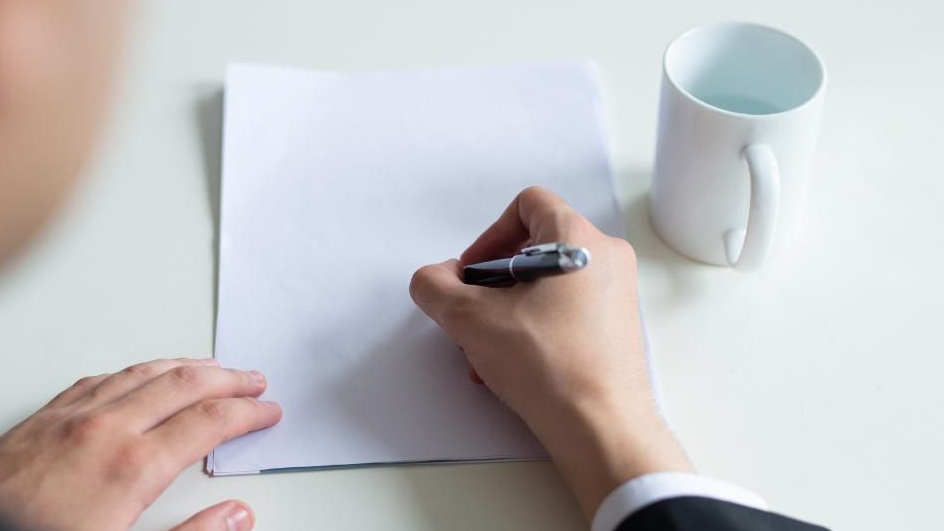 the hands of a man writing on a blank piece of paper