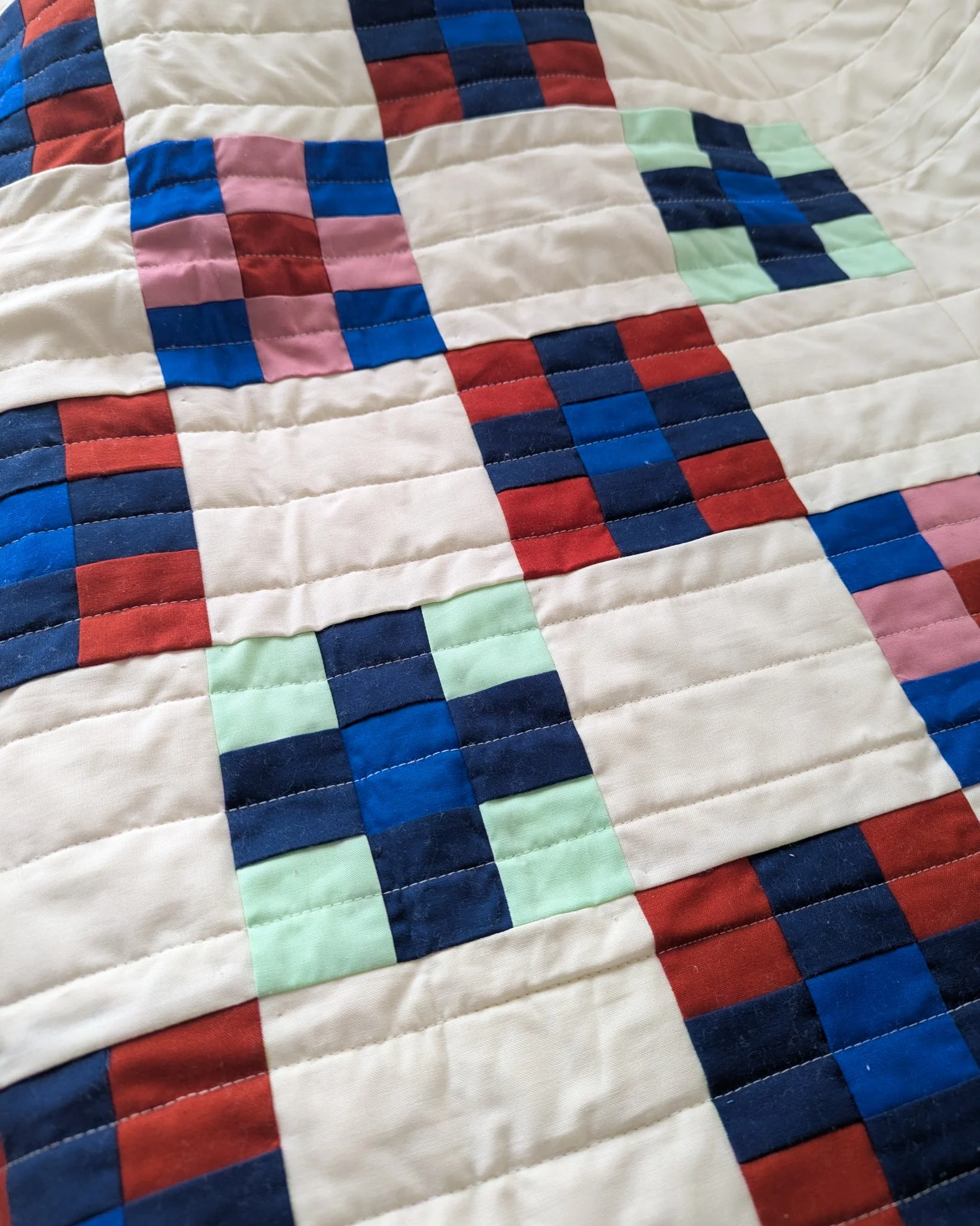 Close-up of a colorful quilt with a geometric pattern of squares and rectangles in red, blue, pink, green, and white.
