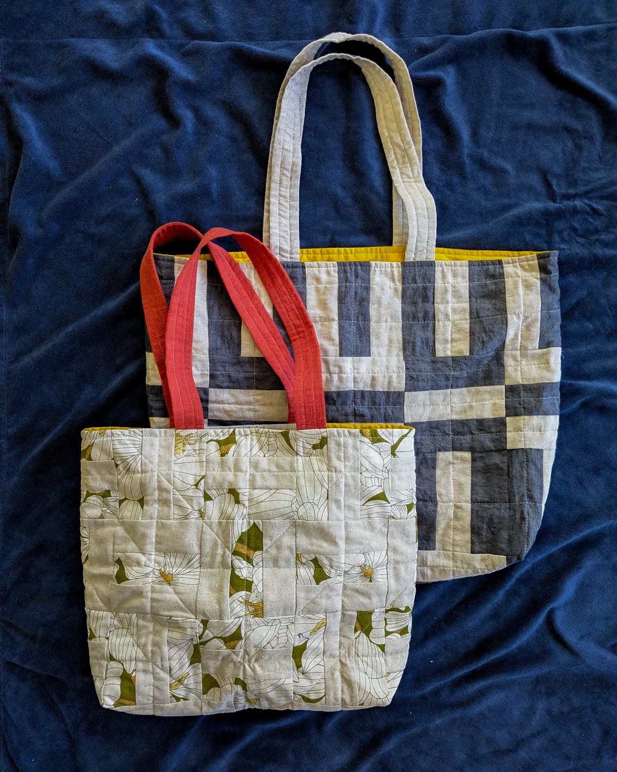 Two quilted tote bags with fabric handles resting on a navy blue fabric surface.