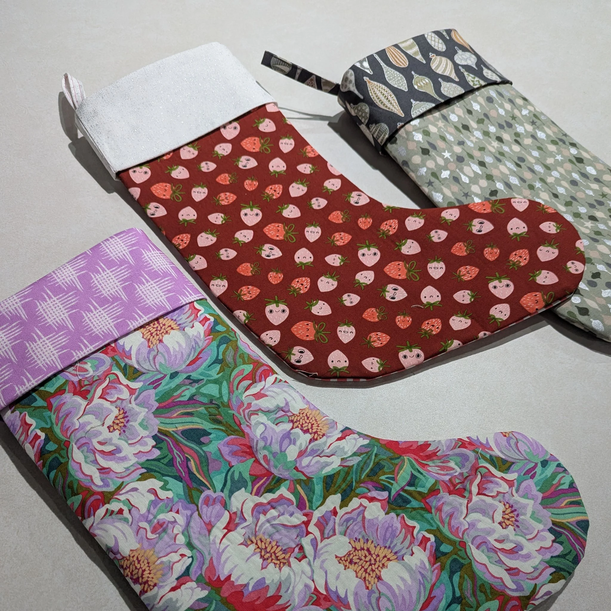 Four decorative stockings with various patterns, including strawberries, leaves, flowers, and geometric designs, laid flat on a surface.