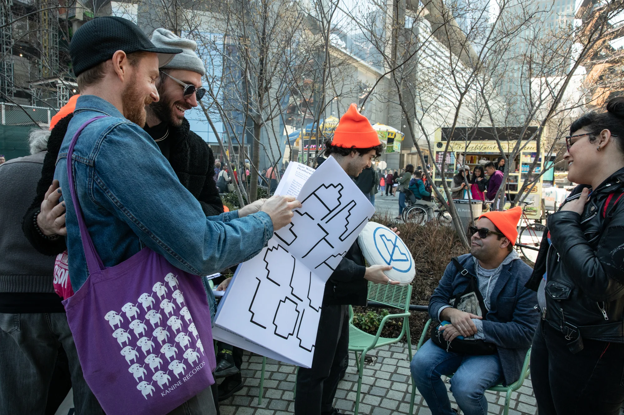 Kevin Gotkin and a friend look at a newspaper together. In the background, Ezra Benus, Jordana Bernstein, and Kevin Quiles Bonilla look at a cushion.