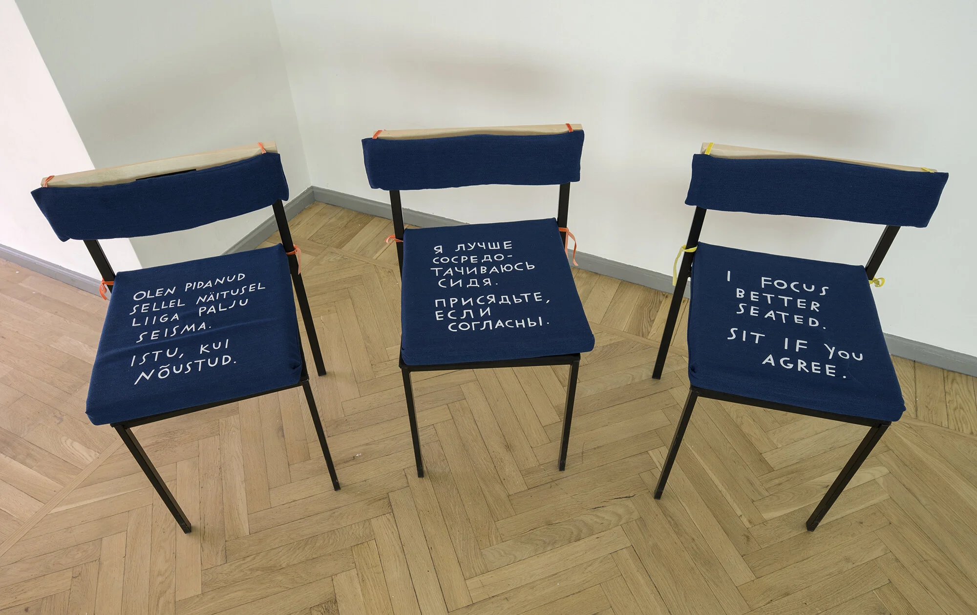 Another set of three chairs, arranged in a slight arc. One has Russian text, one has Estonian, and one has English. The English text reads, “I focus better seated. Sit if you agree.”