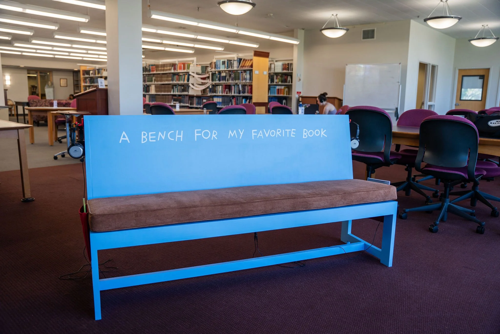 A light blue bench with text across it that says “A bench for my favorite book” in my handwriting. Brown corduroy seat cushion.