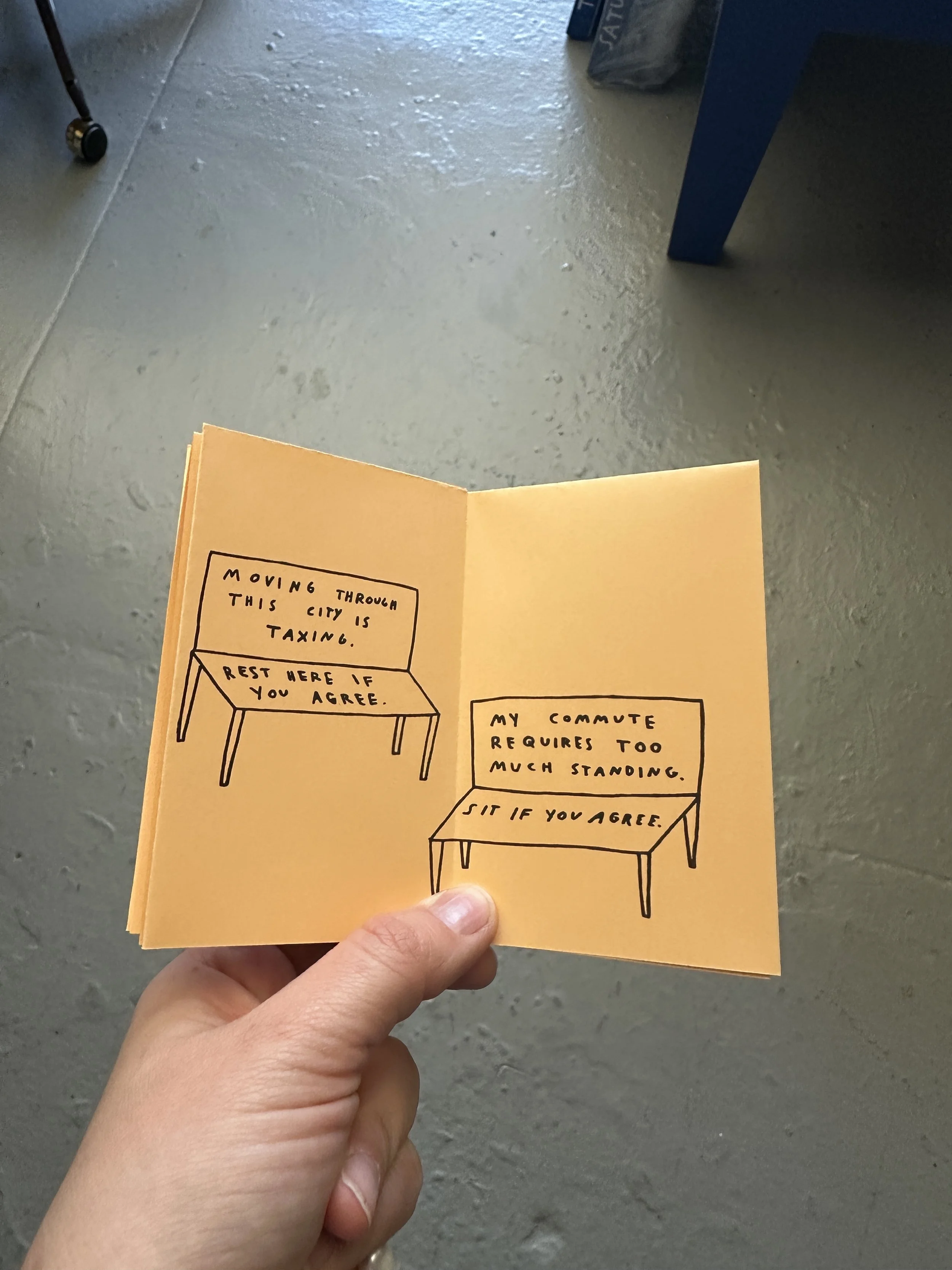 The same zine opened to the center spread with simple line drawings of two benches. One reads “Moving through this city is taxing. Rest here if you agree” and the other, “My community requires too much standing. Sit if you agree.”