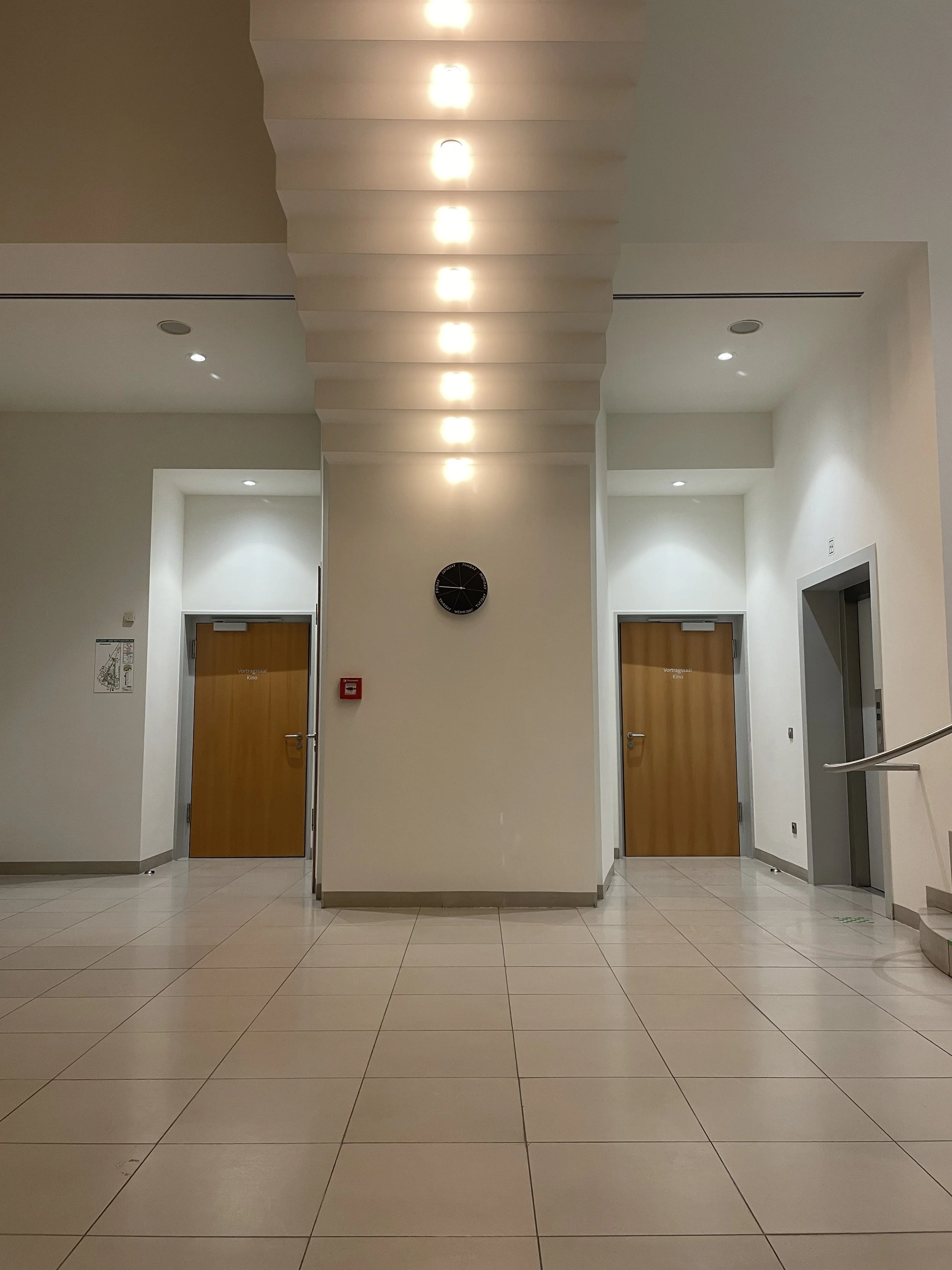 A small black clock hung underneath a stairwell between two doors.
