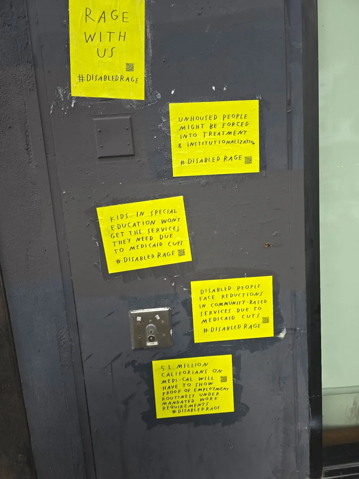 Four bright yellow posters are stacked vertically on a street wall. All with a QR code and #DisabledRage. One says, "RAGE WITH US" while others are about unhoused people, special education and medicaid cuts