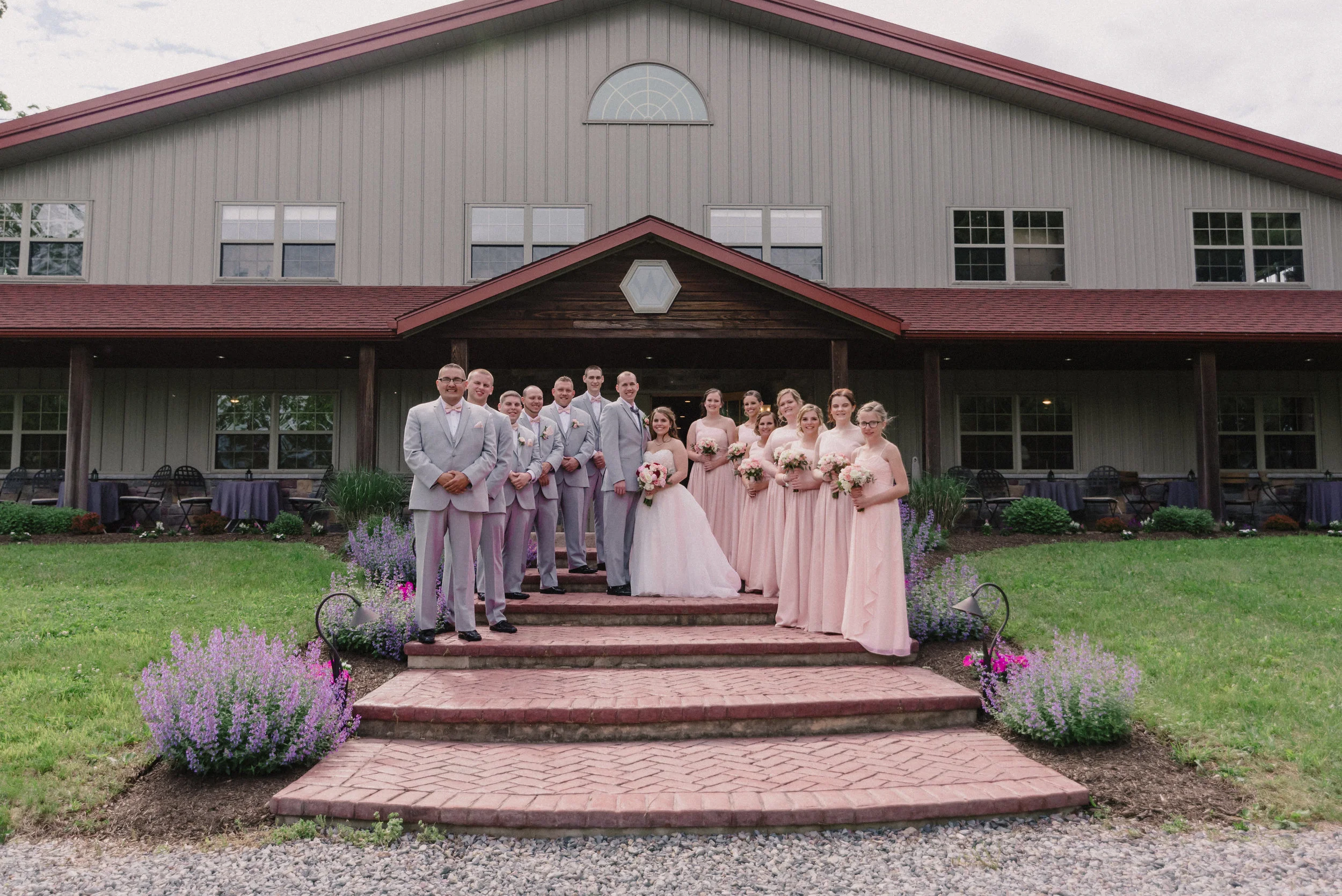 Bridal party poses for the first husband and wife photos in front of the WoodsEdge Farm Wedding and Event Barn. The front porch is beautifully landscaped.