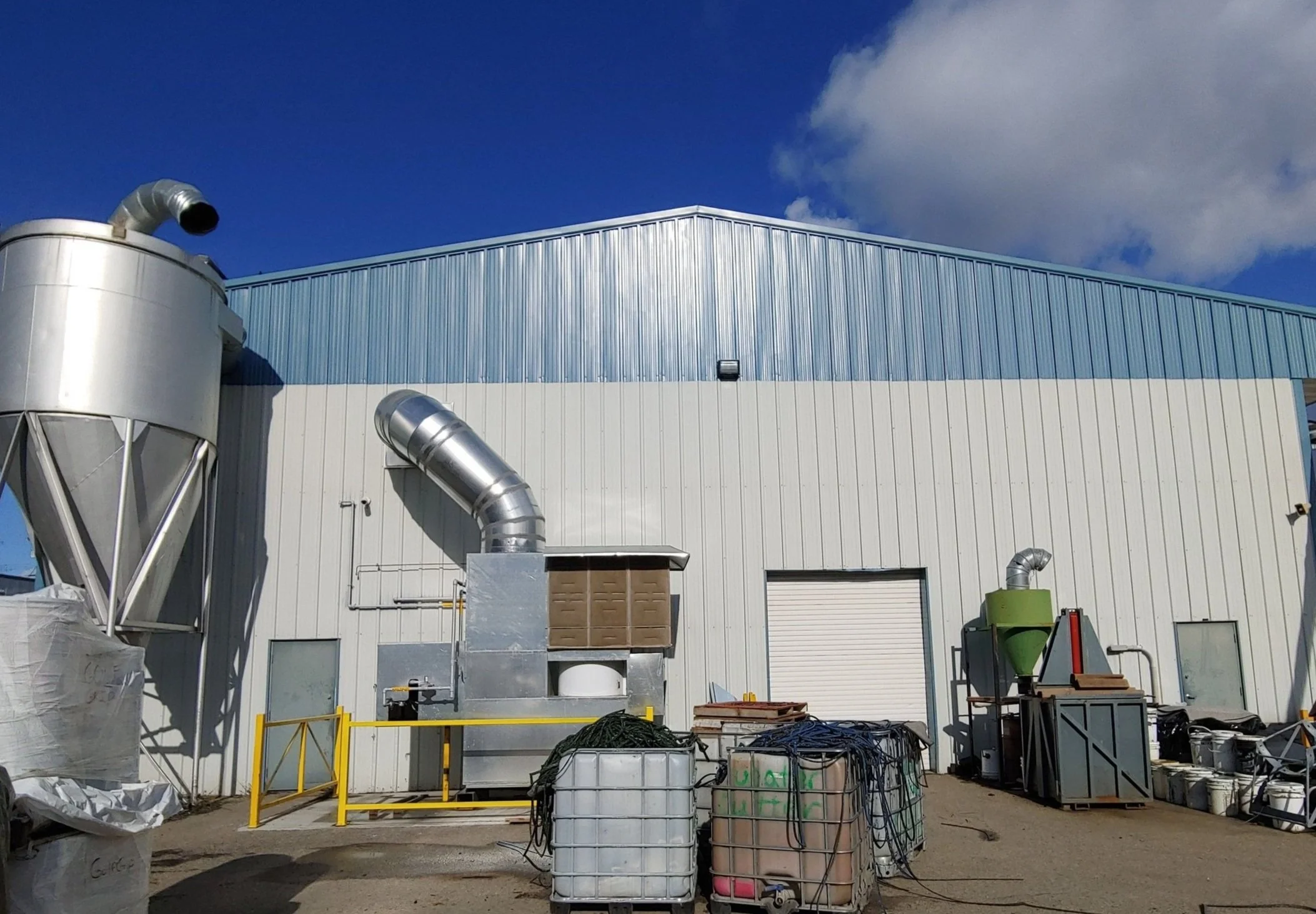 After photo: industrial building exterior side view with freshly painted blue border along roofline and upper panels, light gray metal siding in Okanagan – exterior painting project by Blue Valley Painting