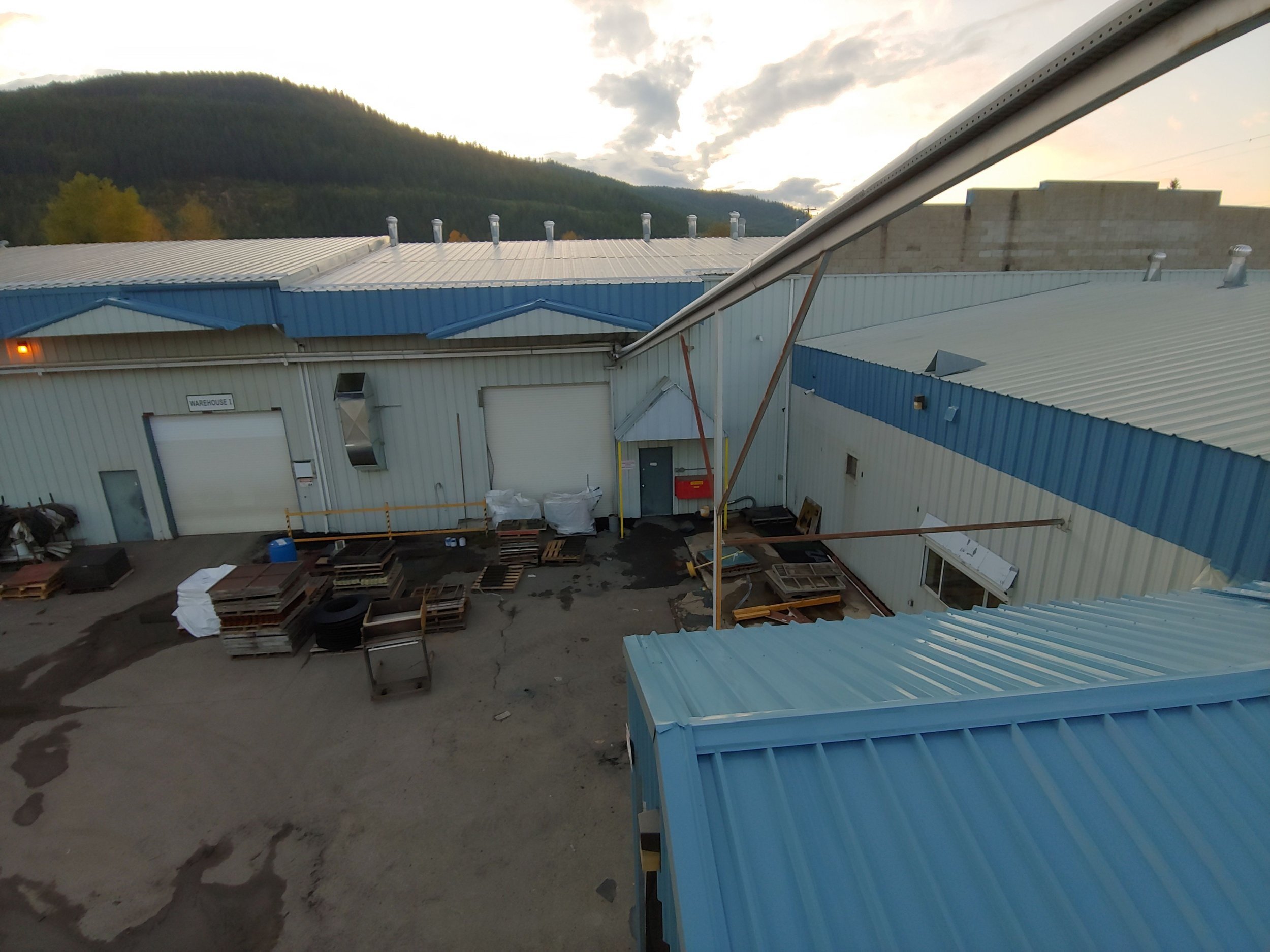 After photo: industrial building exterior overhead view with freshly painted blue border along roofline and upper metal panels, Salmon Arm BC – exterior painting project by Blue Valley Painting