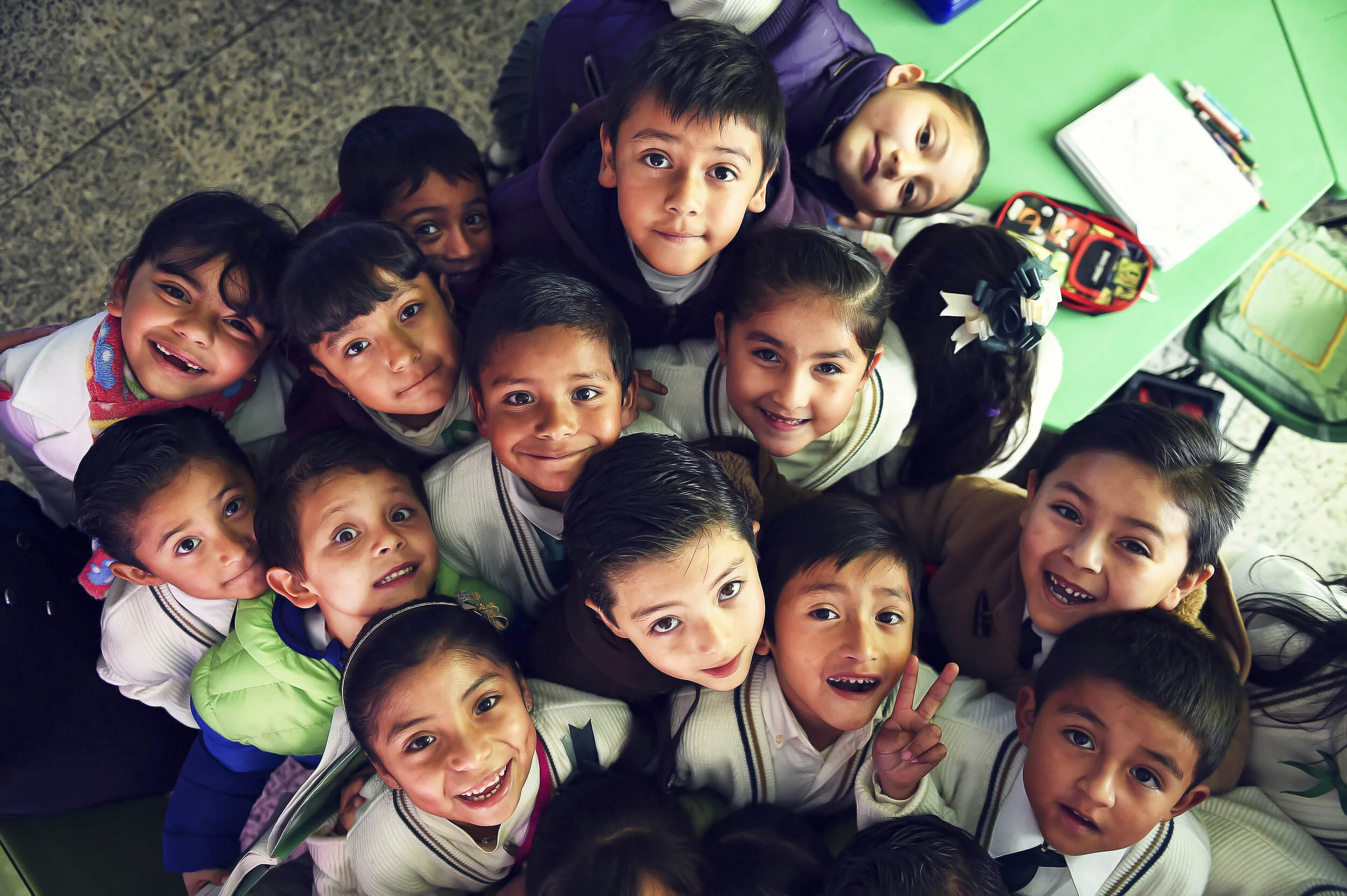 A group of young students in a classroom looking up and smiling at the camera