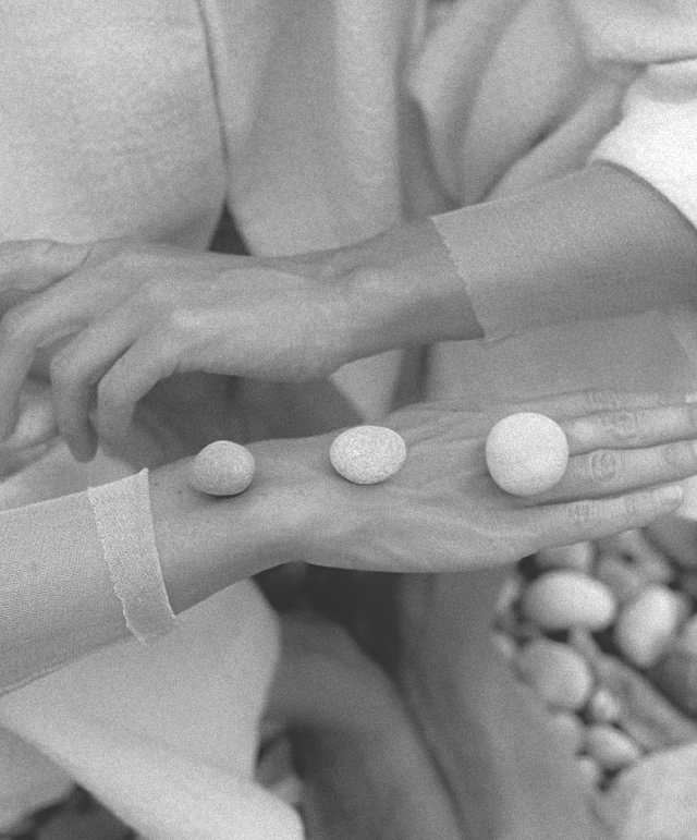 Hands stacked with round objects on the fingers, with additional hands supporting them, in black and white.