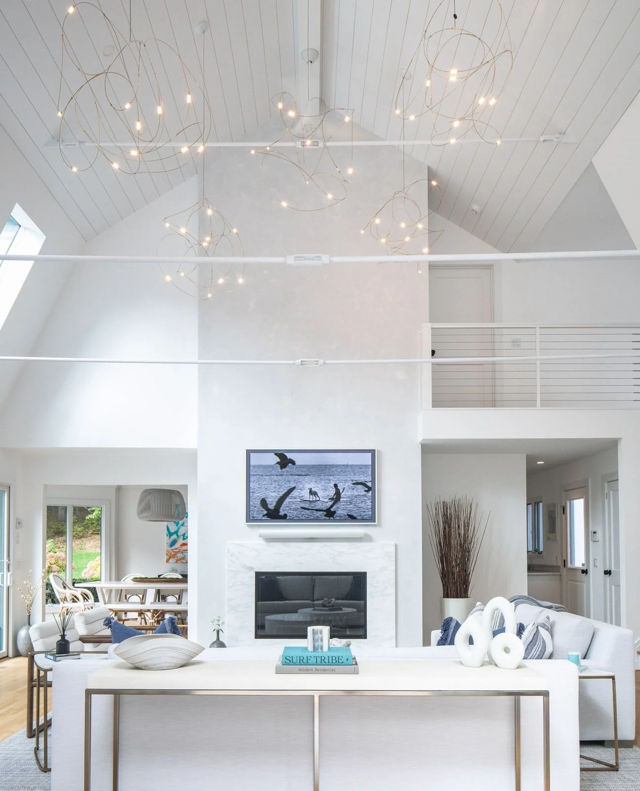 This double-height great room blends sculptural lighting, soft textures, and natural tones to create a serene yet elevated space. The fireplace anchors the room, while every detail was chosen to invite calm and conversation.
