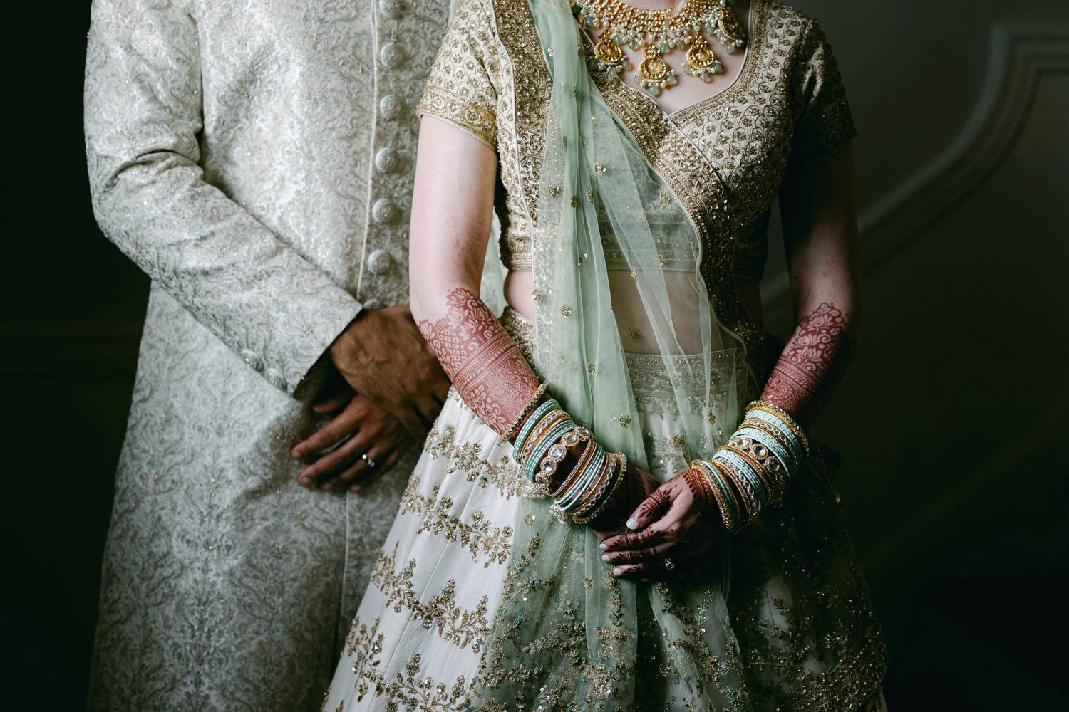 Close-up of a bride and groom in traditional Indian wedding attire, with the bride wearing a heavily embroidered saree and jewelry, and the groom in a matching sherwani.