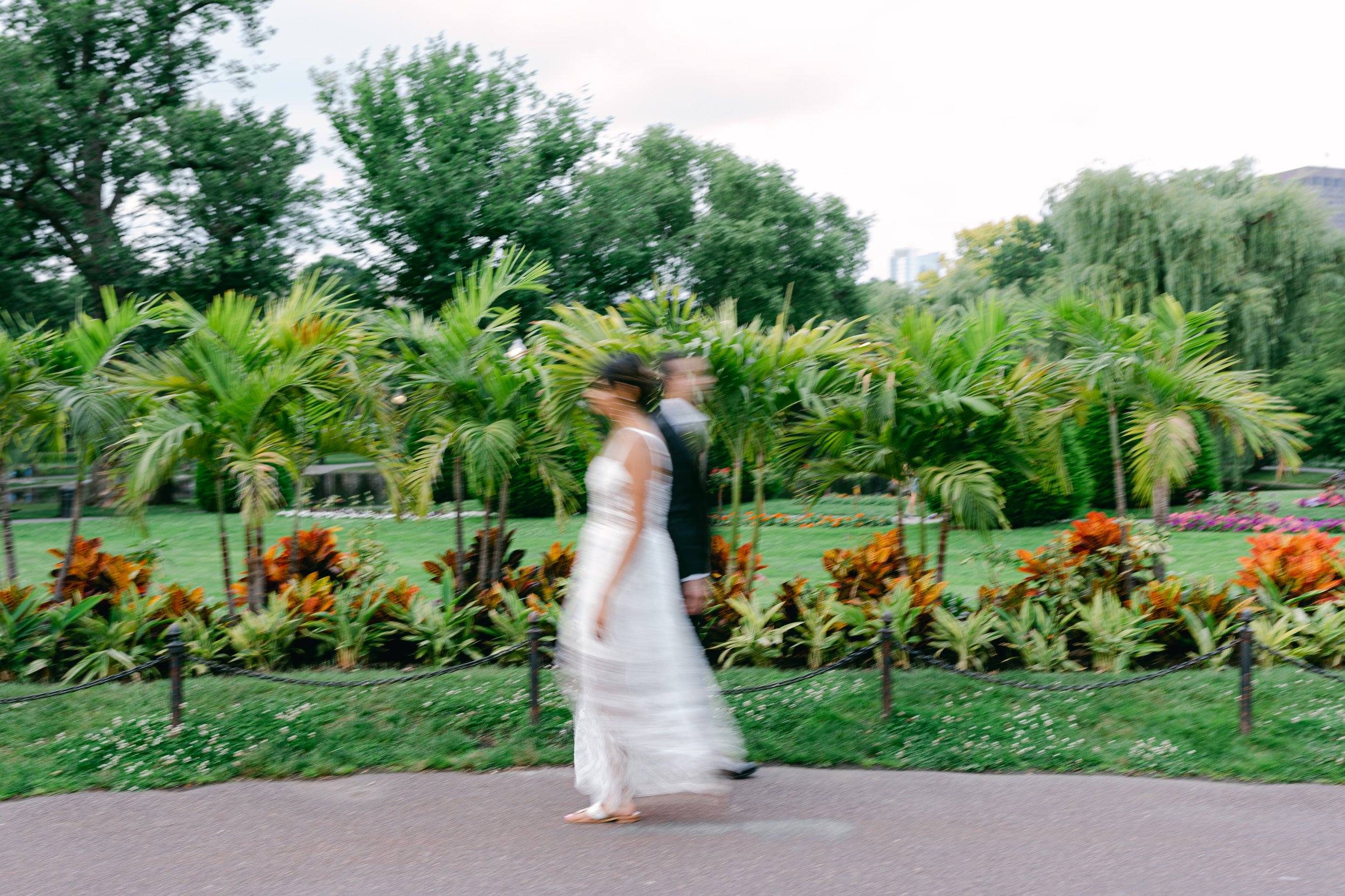 A blurry image of a bride and groom walking in a park with lush greenery and palm trees.