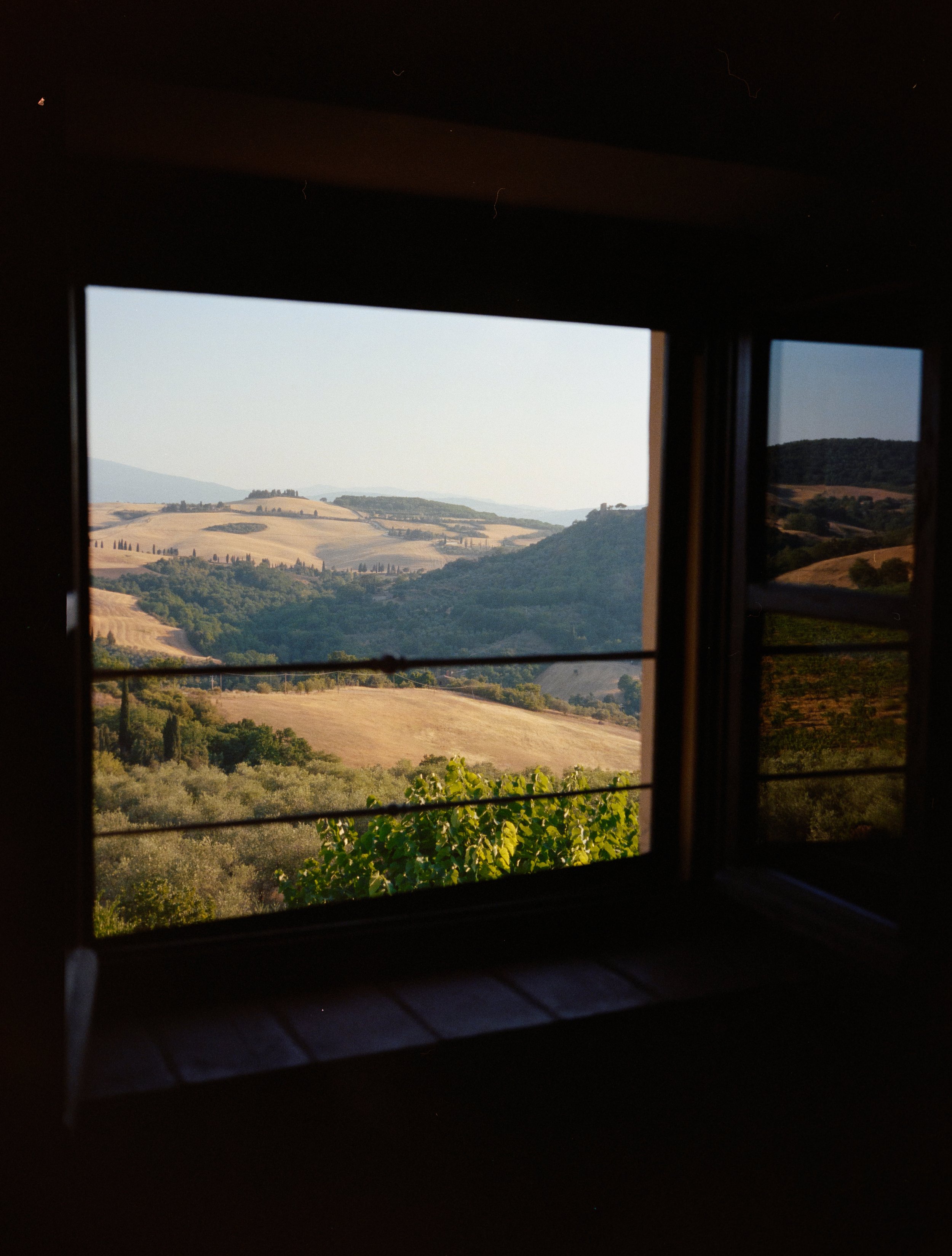 View of rolling hills and fields through an open window.