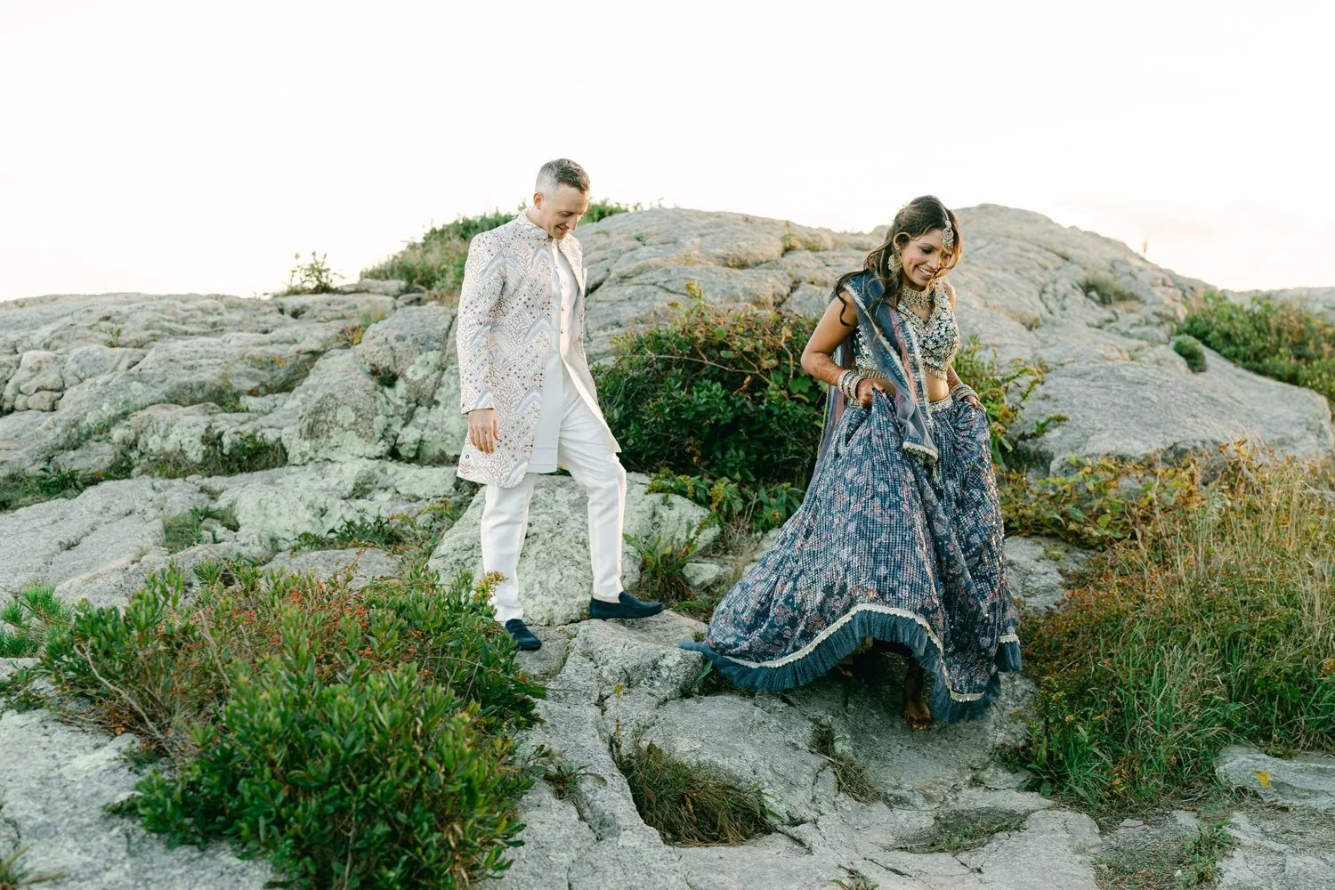 A man and a woman dressed in traditional Indian attire walking on rocky terrain outdoors.