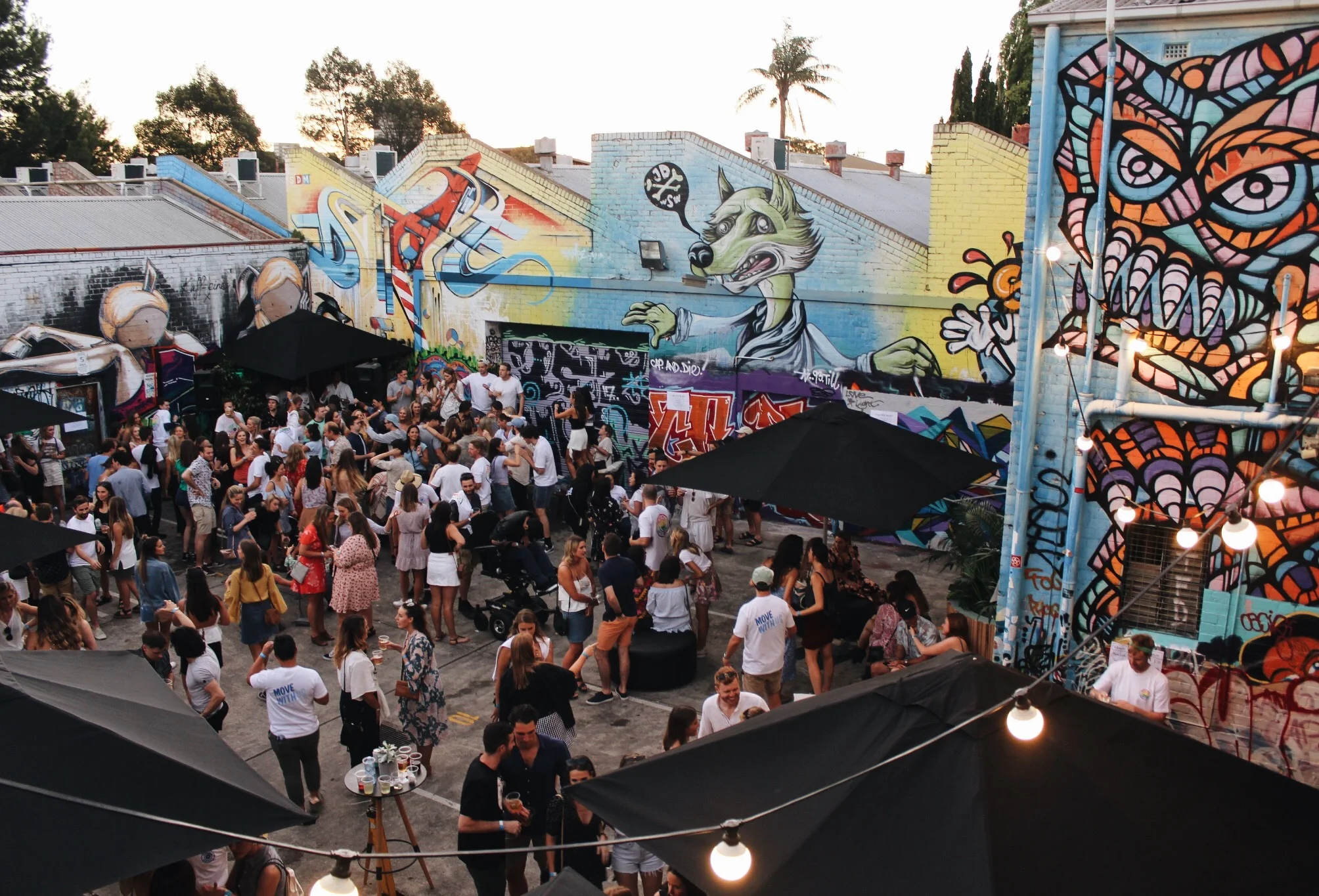 An aerial image of an outdoor party in a laneway with street art and fairy lights